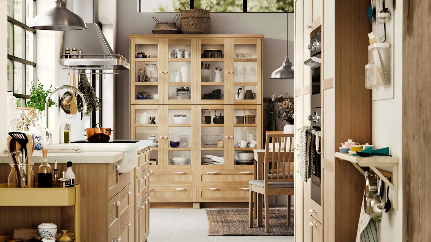 A white and wood kitchen with a glass fronted cabinet filled with kitchen-ware.