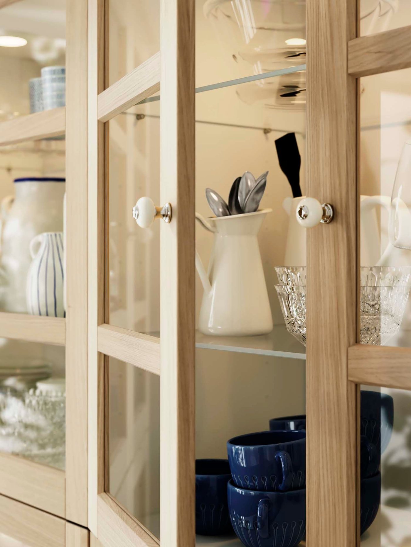 A wood and glass FORSBACKA door is open, revealing a selection of porcelain inside.