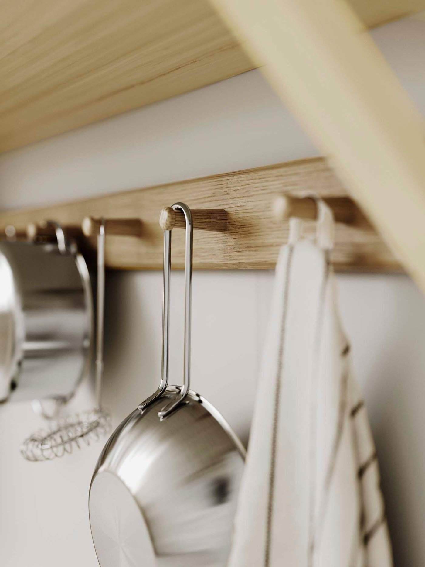Utensils hang from knobs on an oak HÖVHOLM rack mounted on a white wall.
