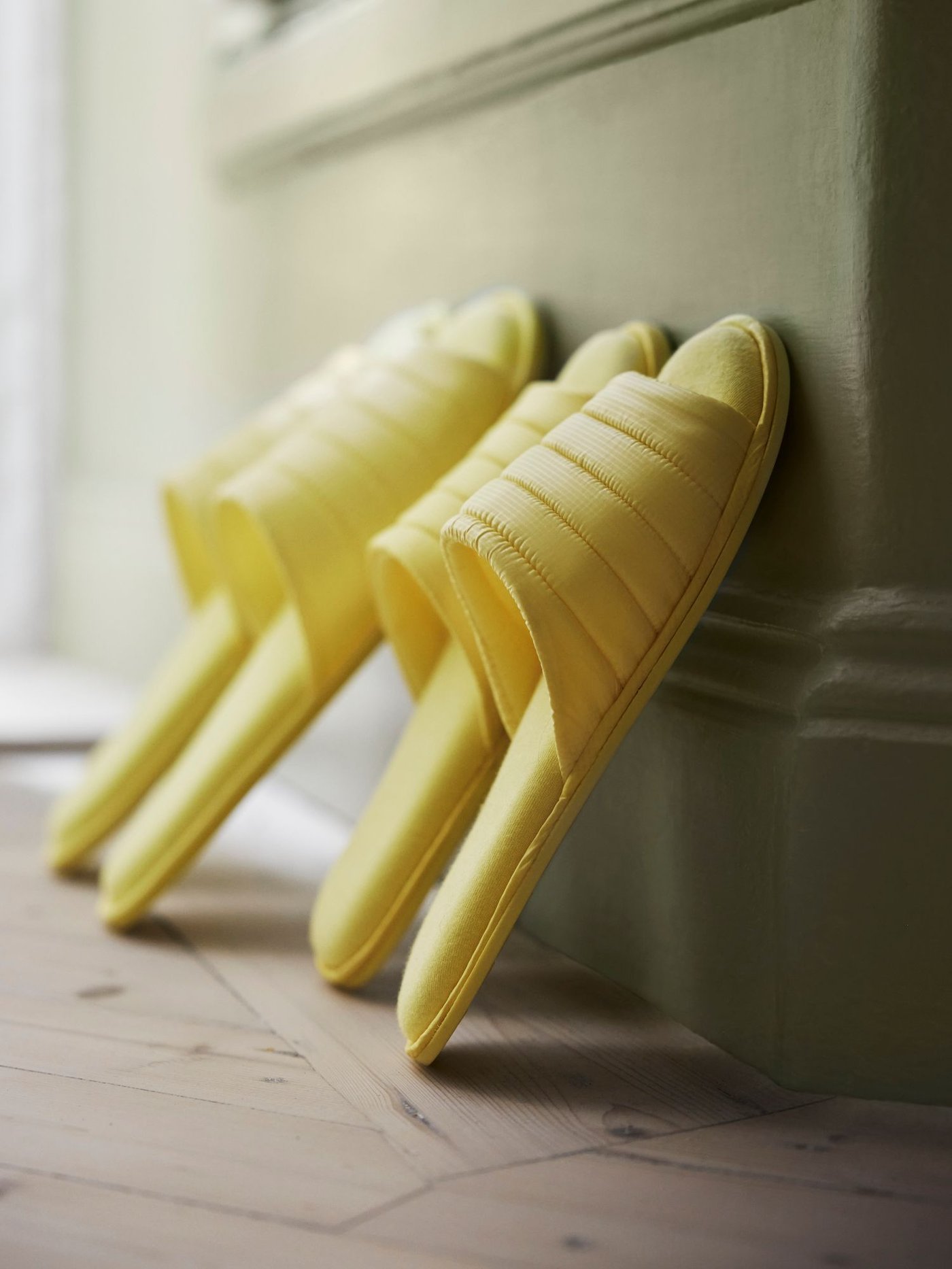 Two pairs of yellow slippers stand perched against a piece of furniture. 