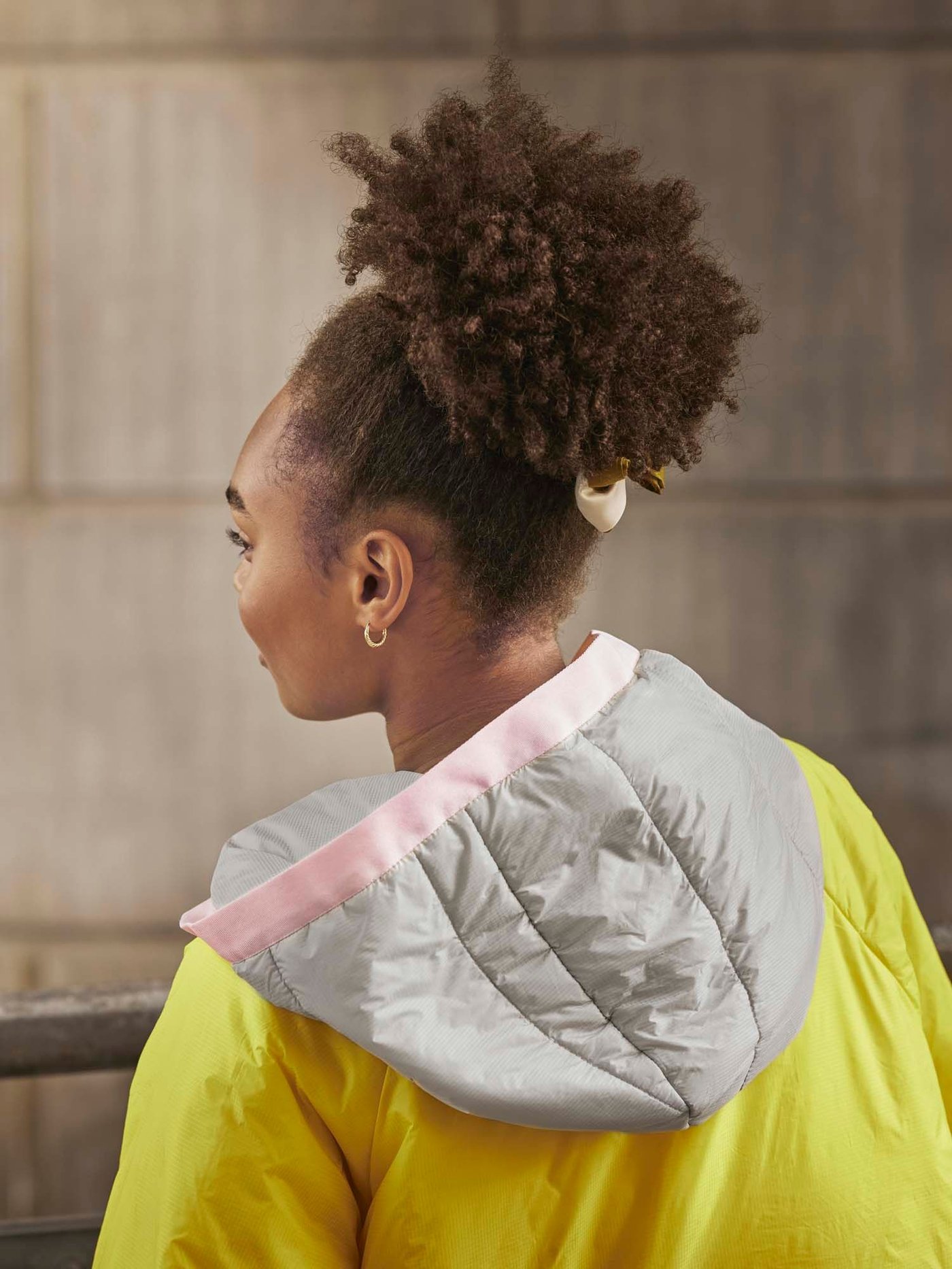 The back of a young woman in a yellow training poncho reveals its grey and pink hood. 