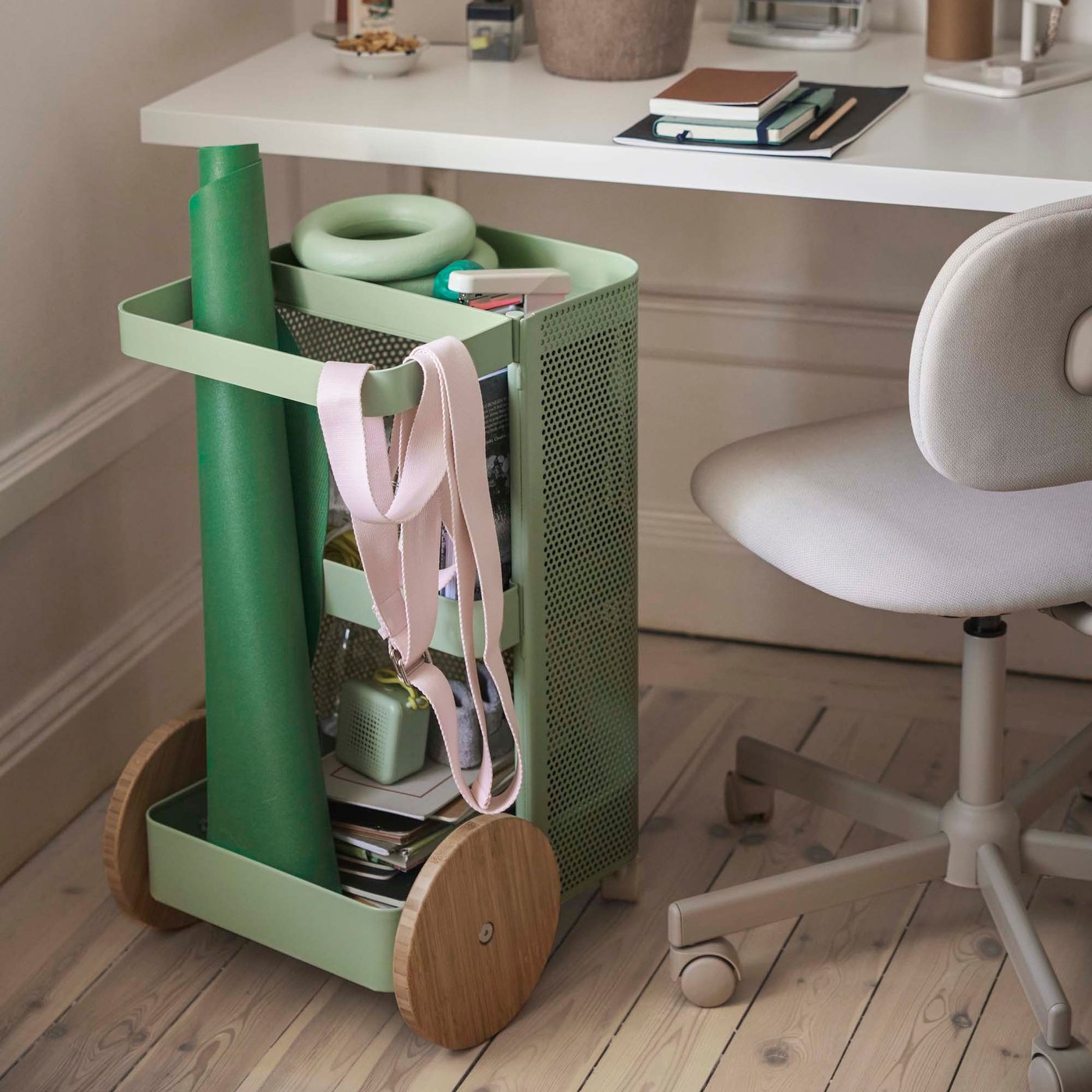 A green trolley filled with the DAJLIEN collection of training equipment, sits underneath a white desk, ready to be rolled out for use.