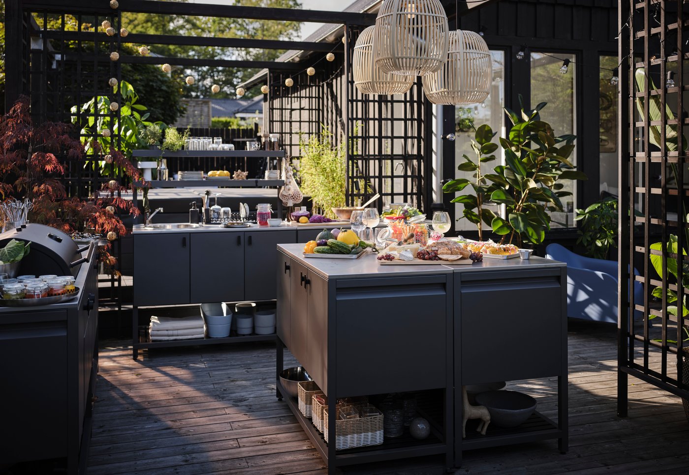 An outdoor terrace featuring an outdoor kitchen with grill, worktop and sink, surrounded by plants.