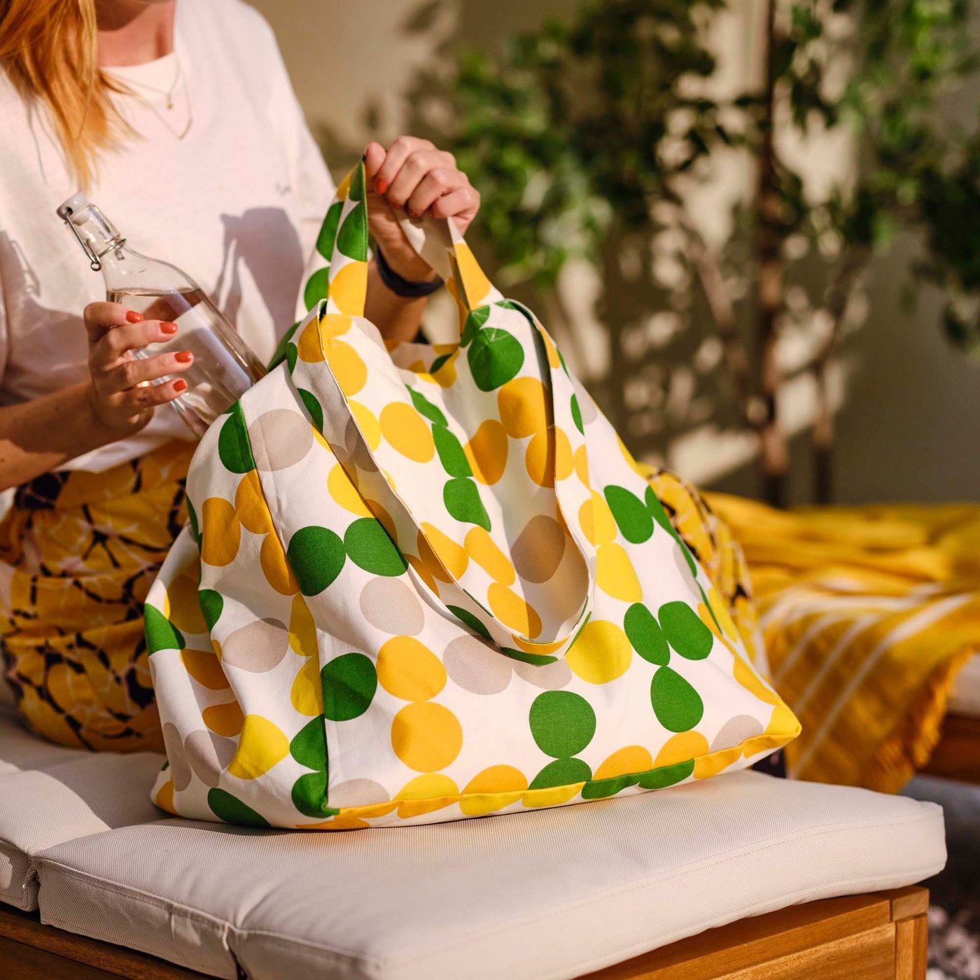 A person putting a drinking bottle into a dot pattern multicolour BRÖGGAN beach bag.