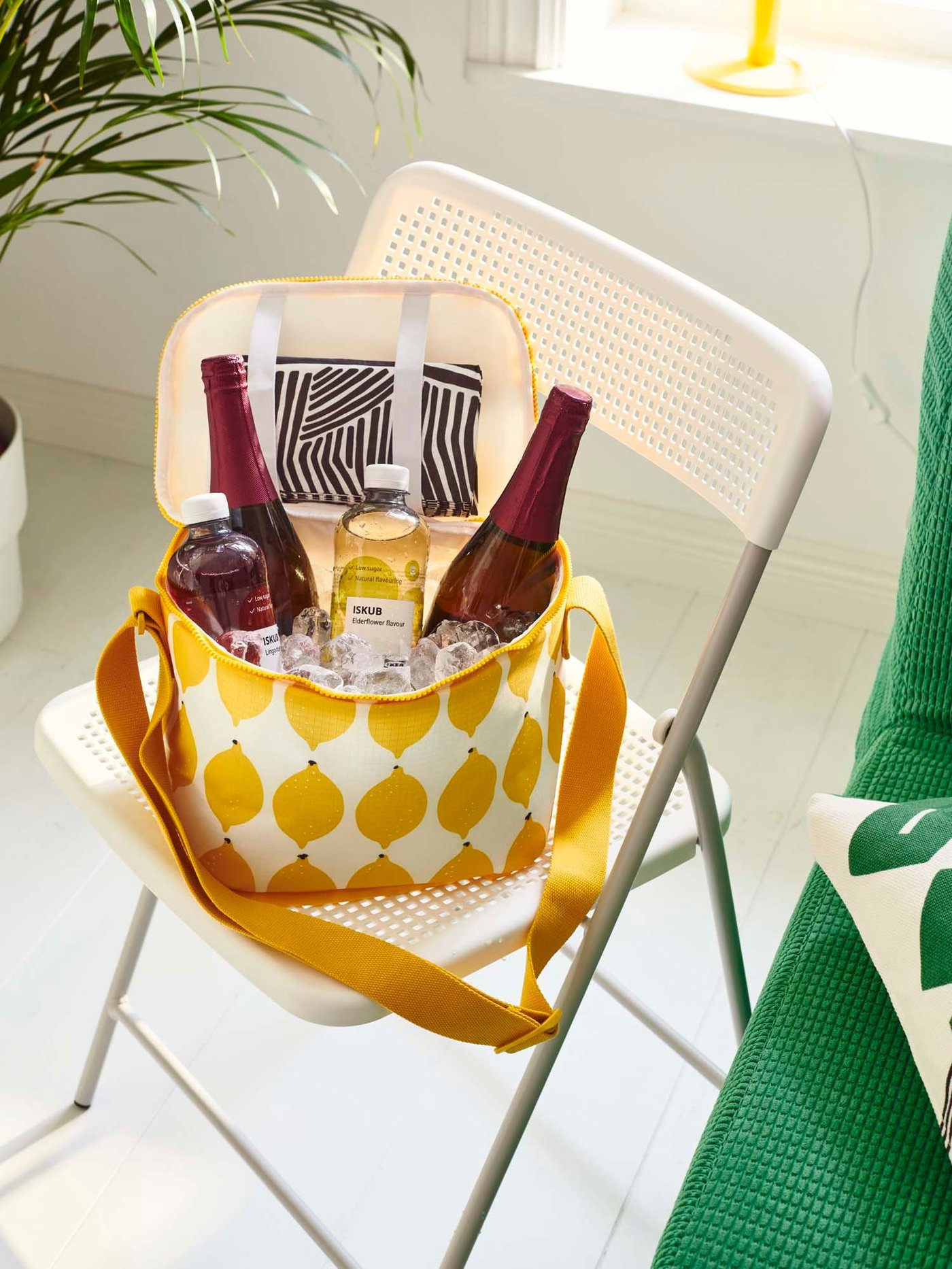 A white/bright yellow patterened NÄBBFISK cooler bag filled with drinks on a white/grey in/outdoor foldable TORPARÖ chair.