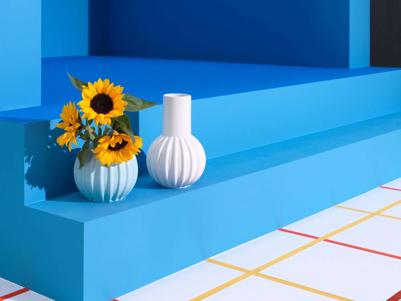 Blue background and small stairs with two white vases, one containing sunflowers.