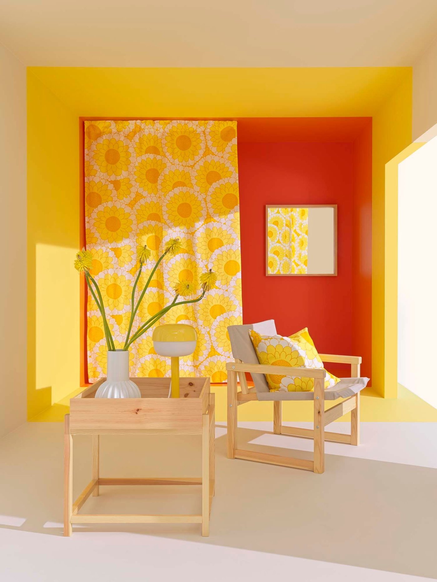 A yellow and orange room, with yellow curtains and an armchair in the background and the PRIMÄRSKOG plant stand with a vase and a yellow lamp on top.