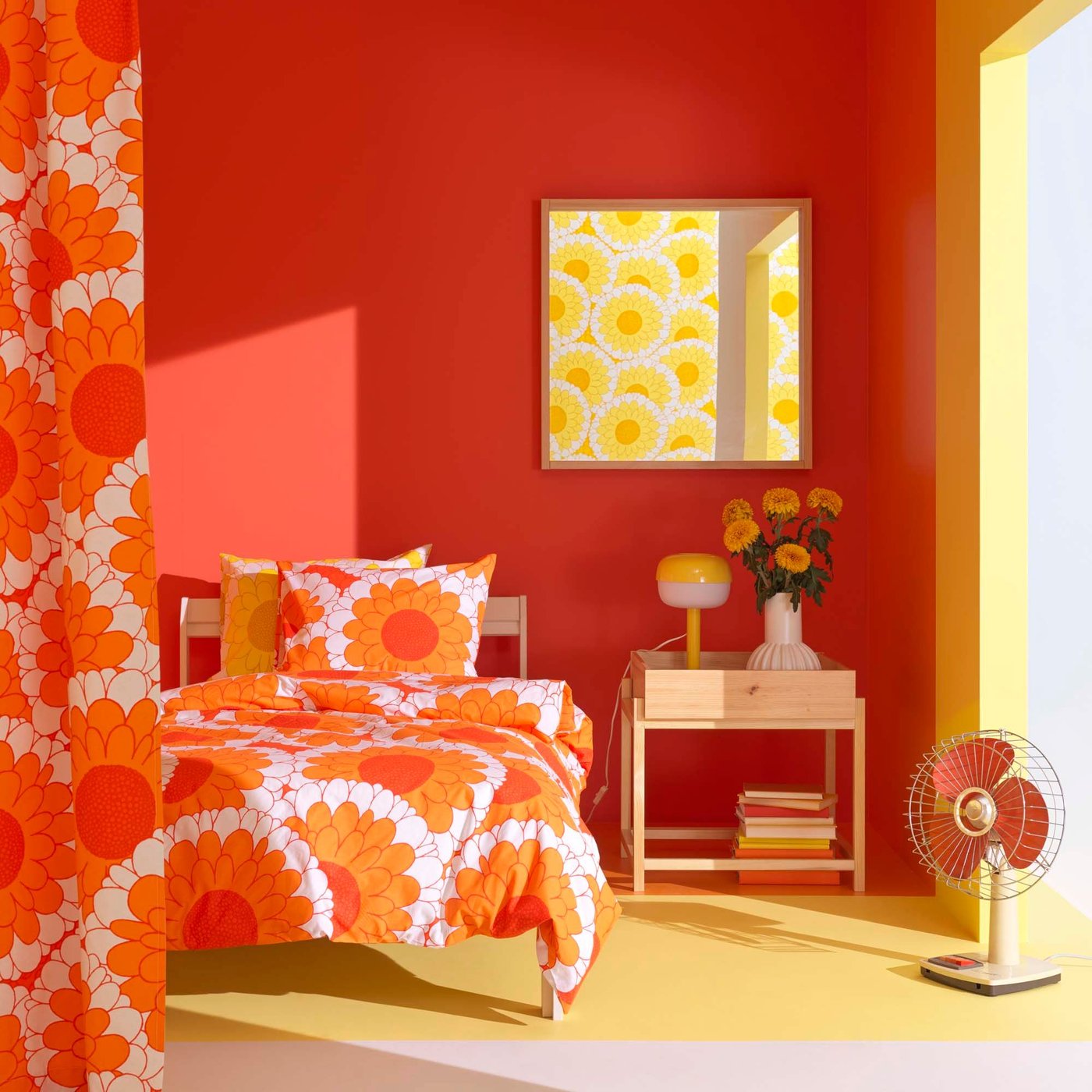 A bedroom with bright orange walls, a bed and a nightstand. The bedding is a bold print of orange flowers on a white background. 