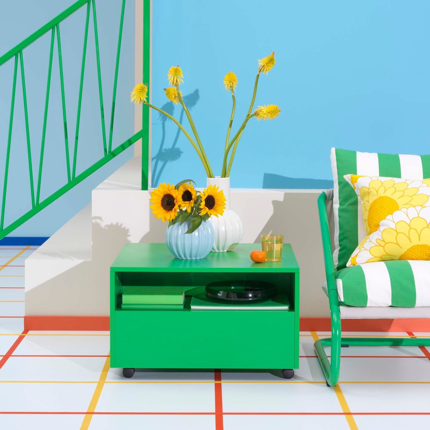 A bright green GARNANÄS coffee table with a vase on top sits next to a striped chair, in front of a blue wall.