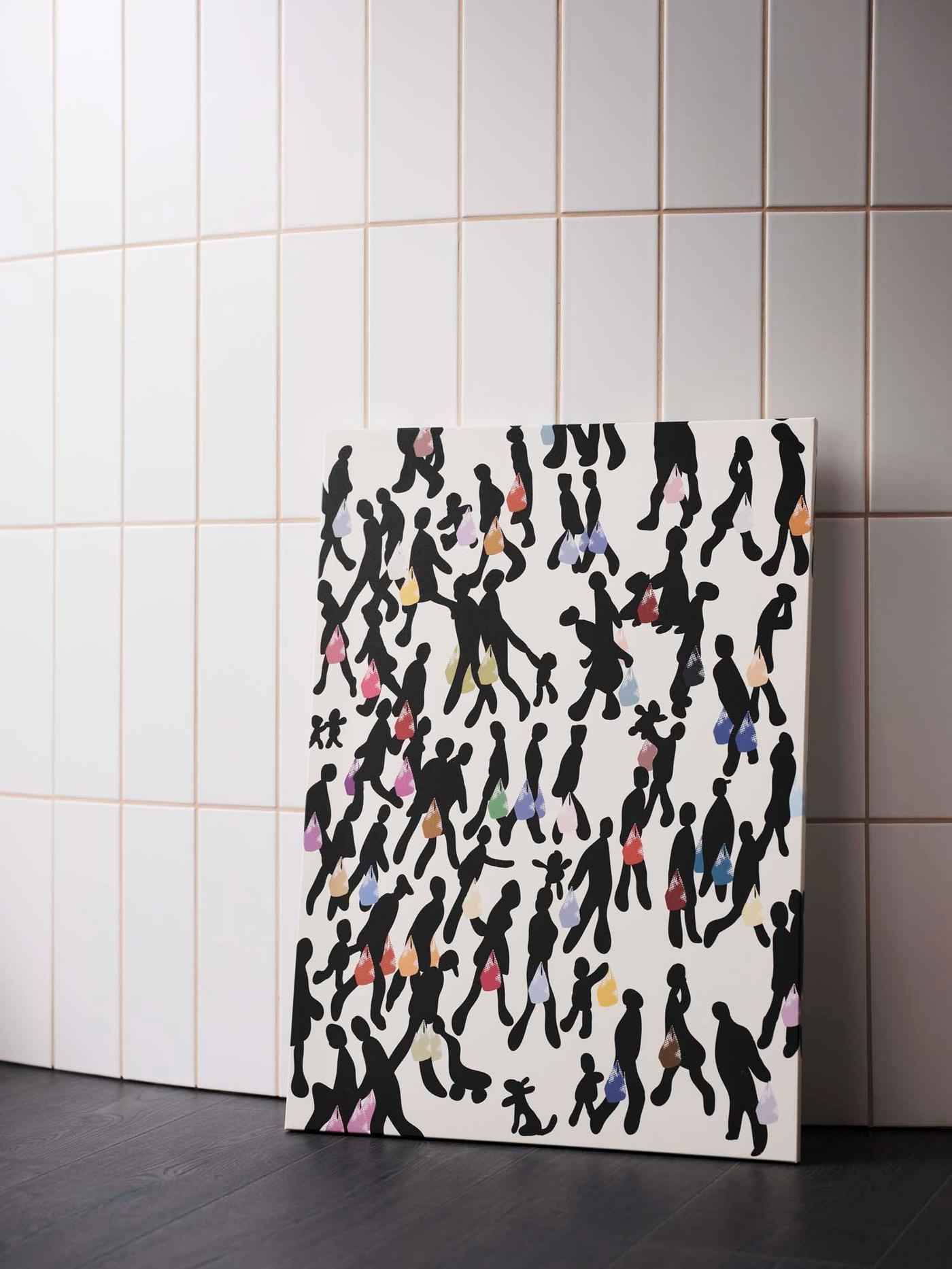A black and white PJÄTTERYD picture stands on a black surface, against a white tiled wall.