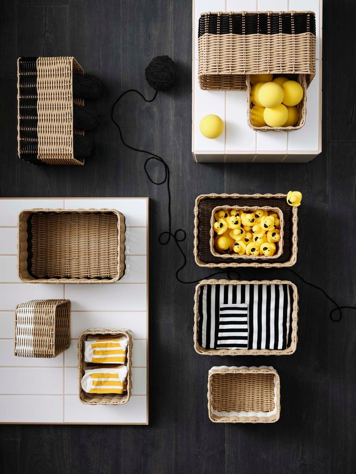 A dark surface with storage boxes in natural materials, filled with yellow or black and white objects.