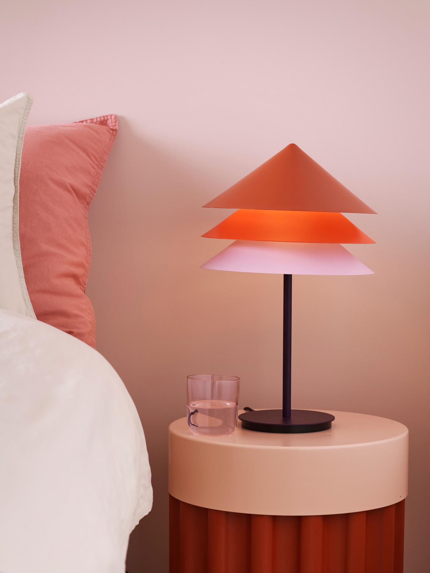 A lamp with three shades of different tones is standing next to a bed on a bed table