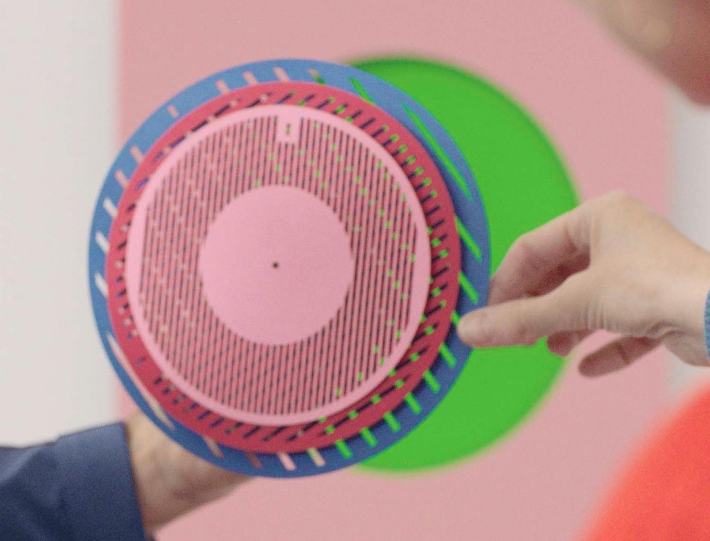 Two hands holding different layers of a paper prototype of the TESAMMANS wall clock.