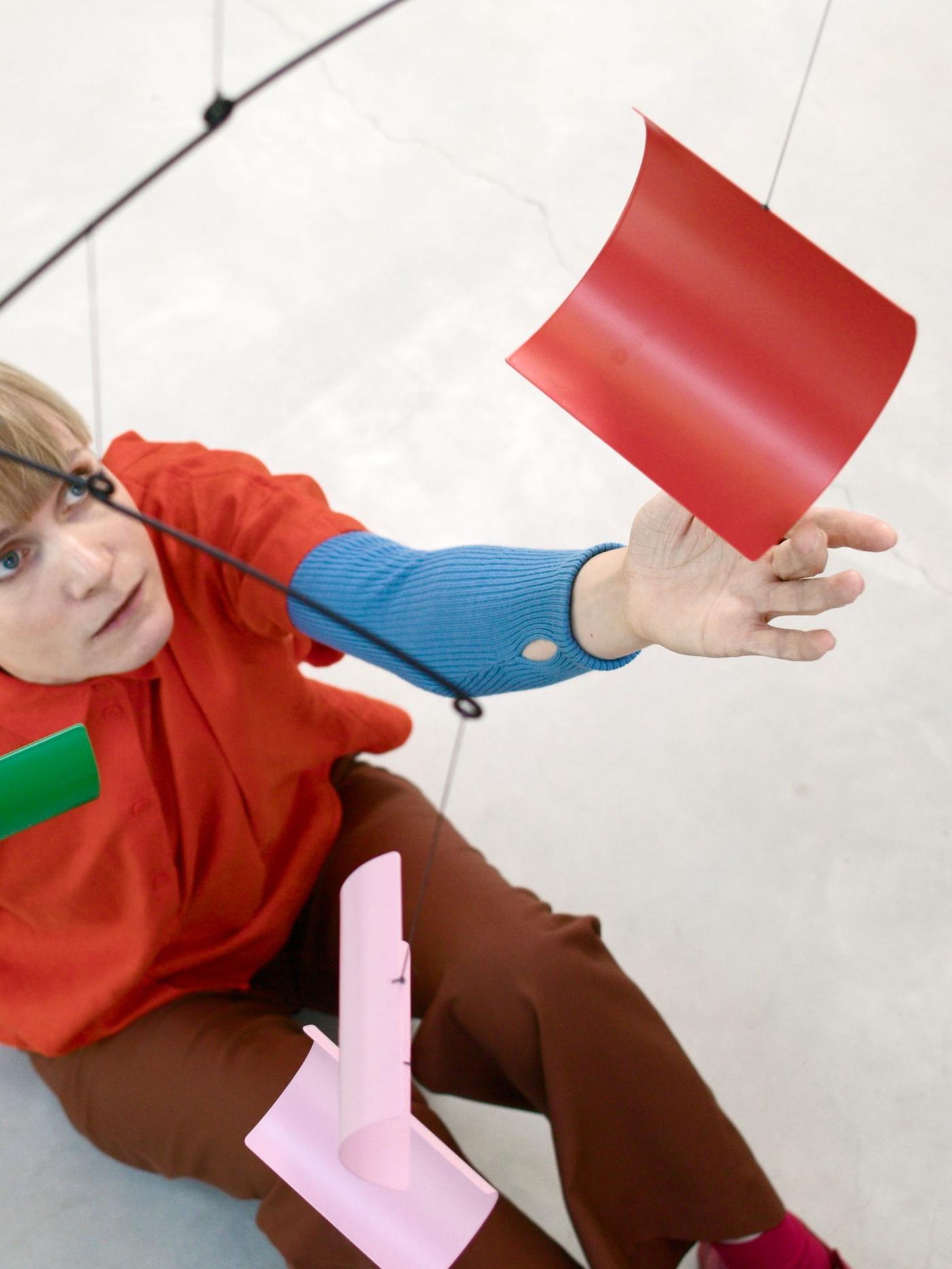 Daniera ter Haar of Raw Color sitting on the floor touching a hanging decoration with her hands..
