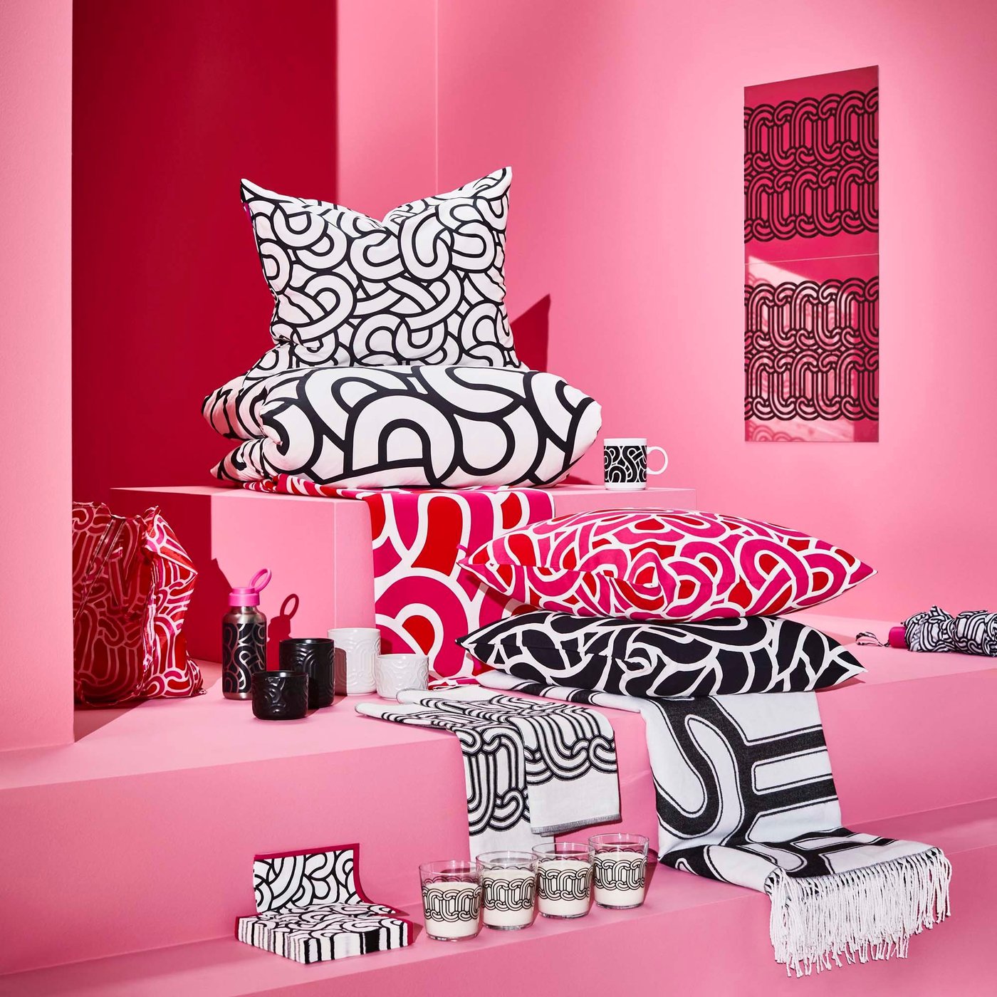 A group of patterned home accessories, such as pillows and napkins, against a pink backdrop.