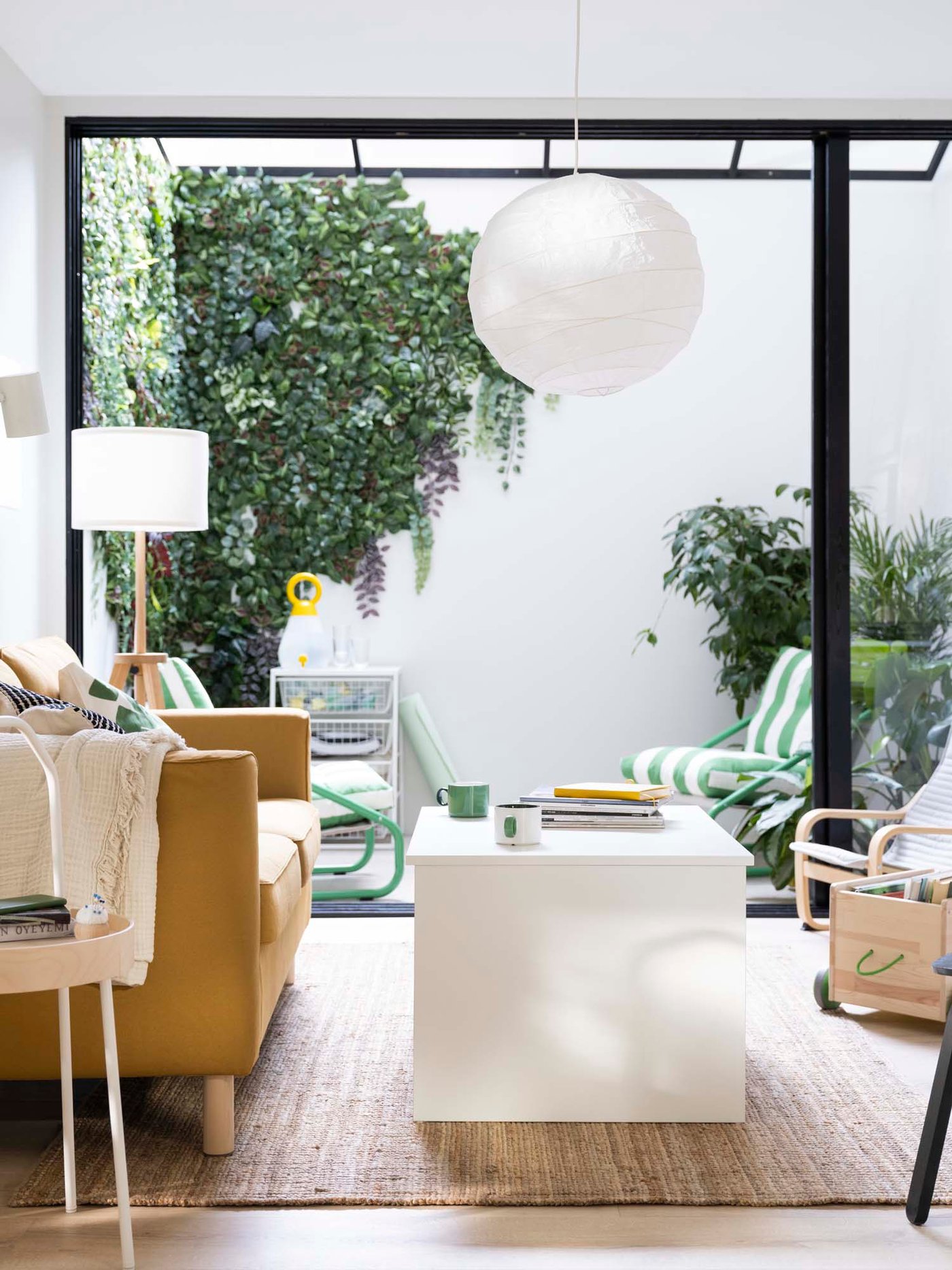 View from a living room, looking out to a modern terrace or conservatory, with FEJKA green lilac on the walls and plants in the corner.