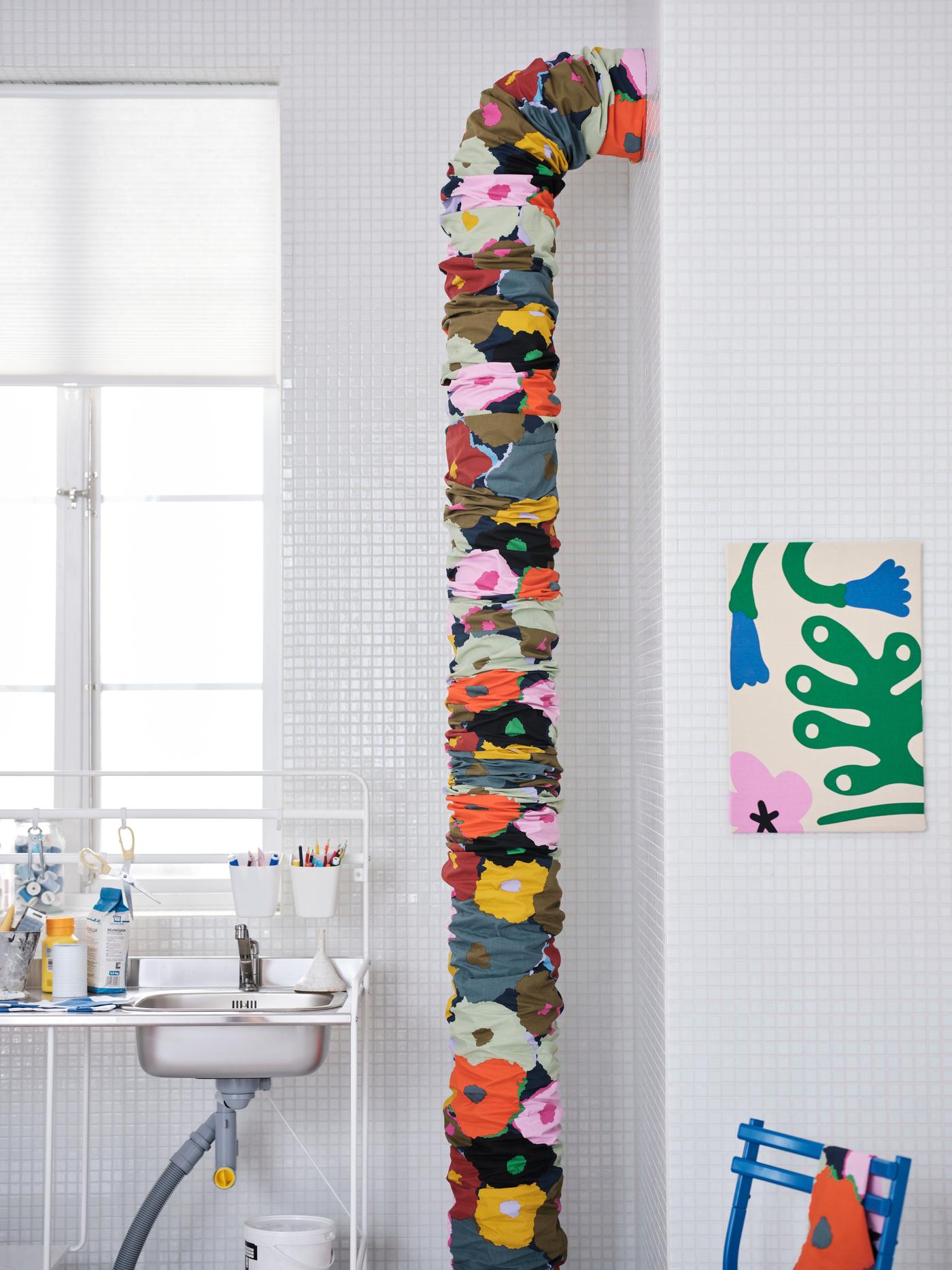 There is a pipe that is covered with floral patterned fabric; on the wall, there is also a frame covered with fabric. 