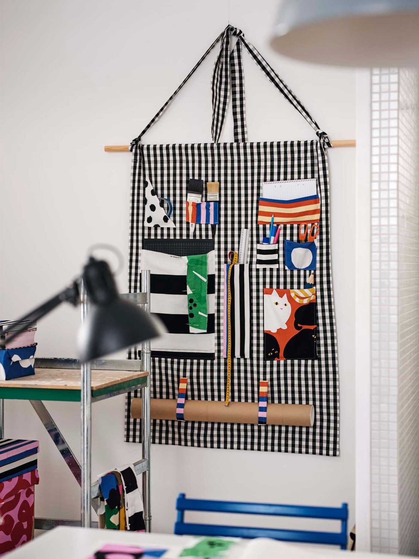 A hand made organiser in striped and check fabric hangs from a wall.