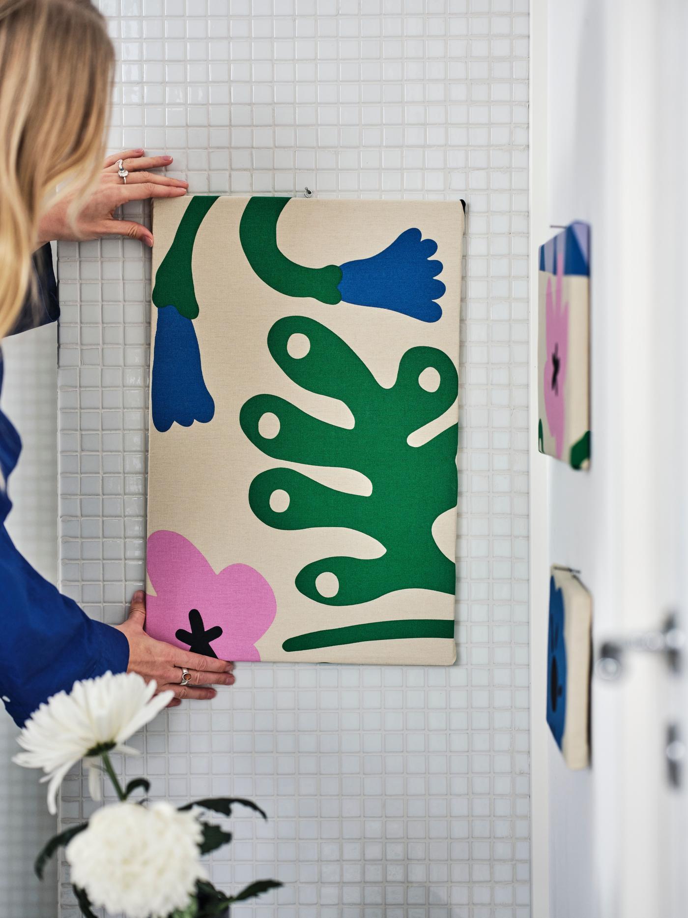 A person is hanging a frame on the wall made of abstract pattern fabric.