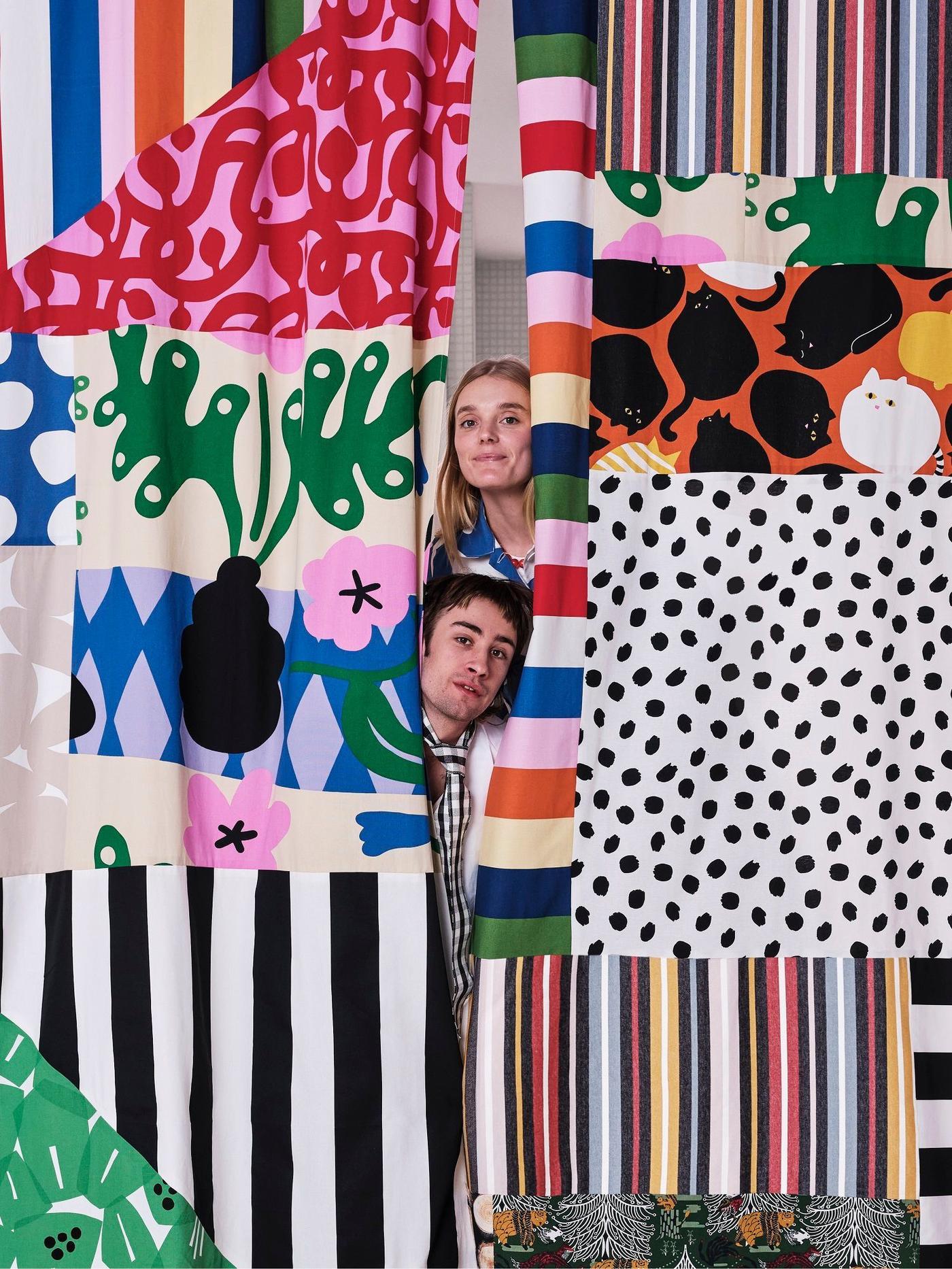 Two people are sneaking peak through a big collage of fabrics.