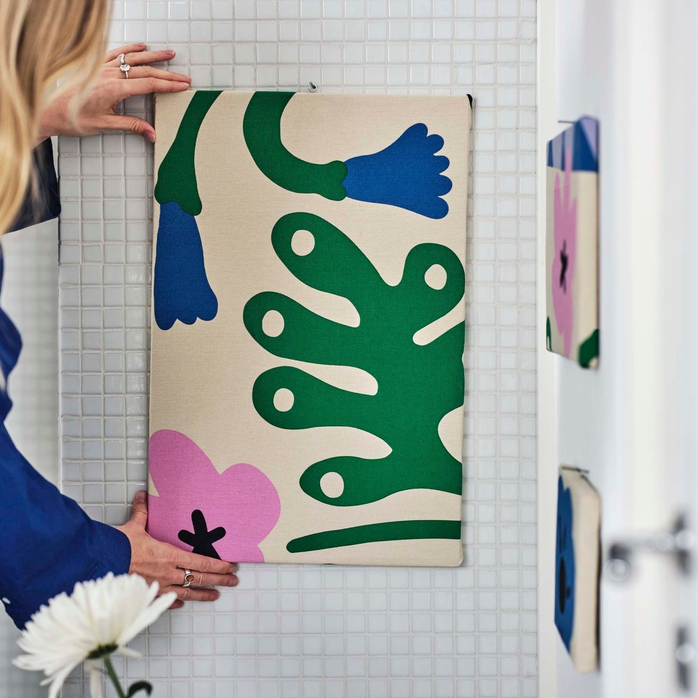 A person hands a piece of fabric stapled onto a canvas onto a wall. 