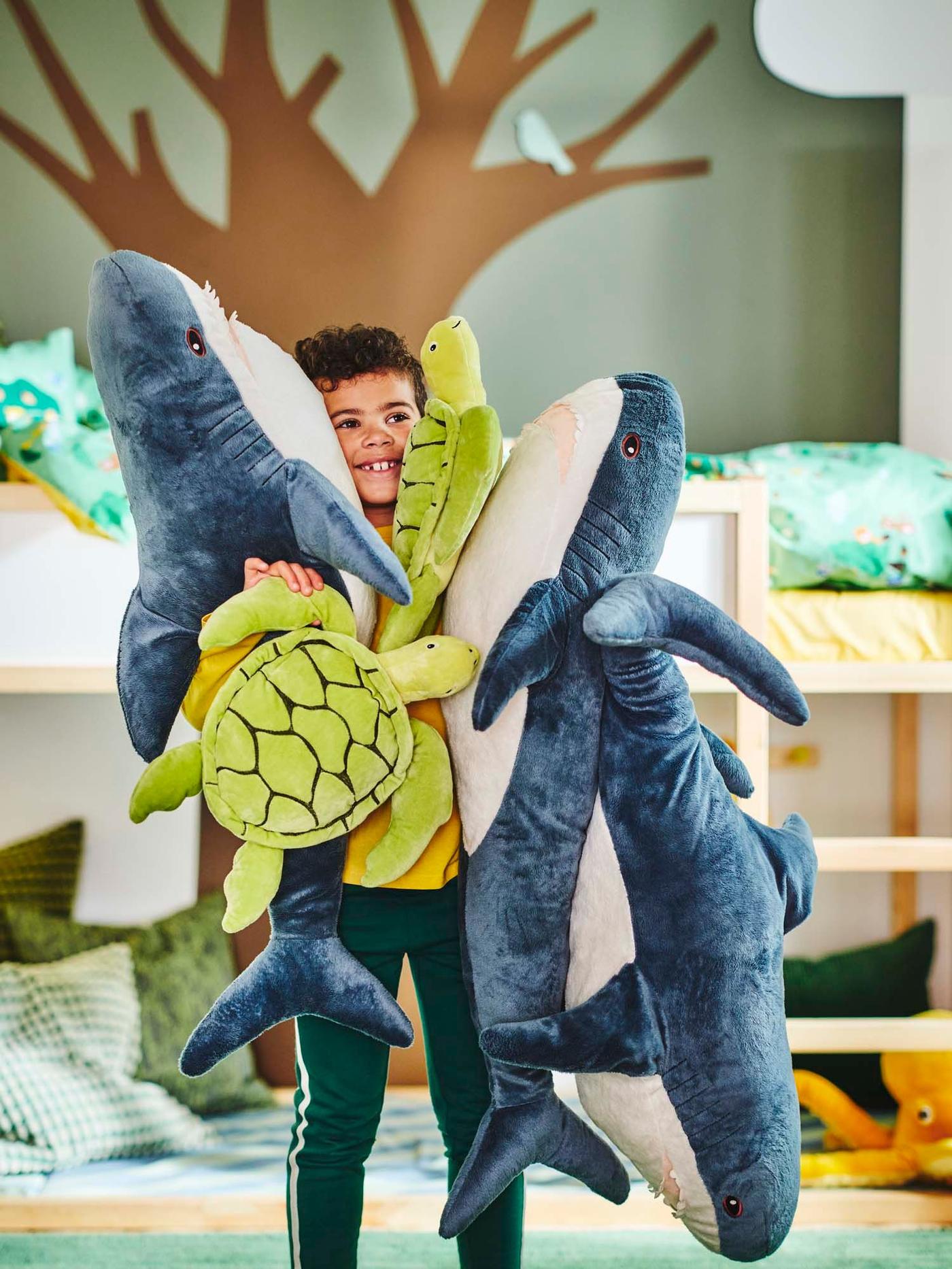 A child hugging a collection of ocean-inspired stuffed toys.