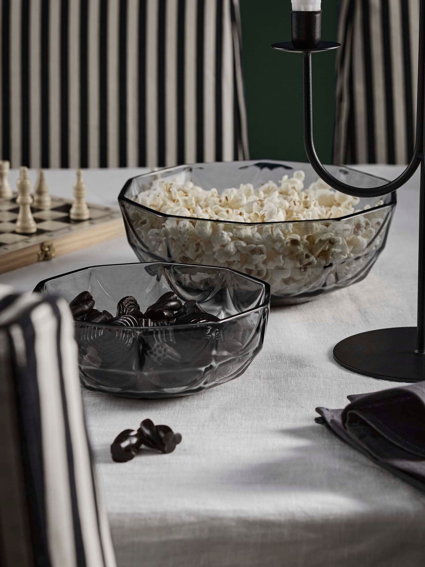 A table with two grey HÖSTAGILLE bowls filled with popcorn and liquorice atop a white KLYVBLAD tablecloth.
