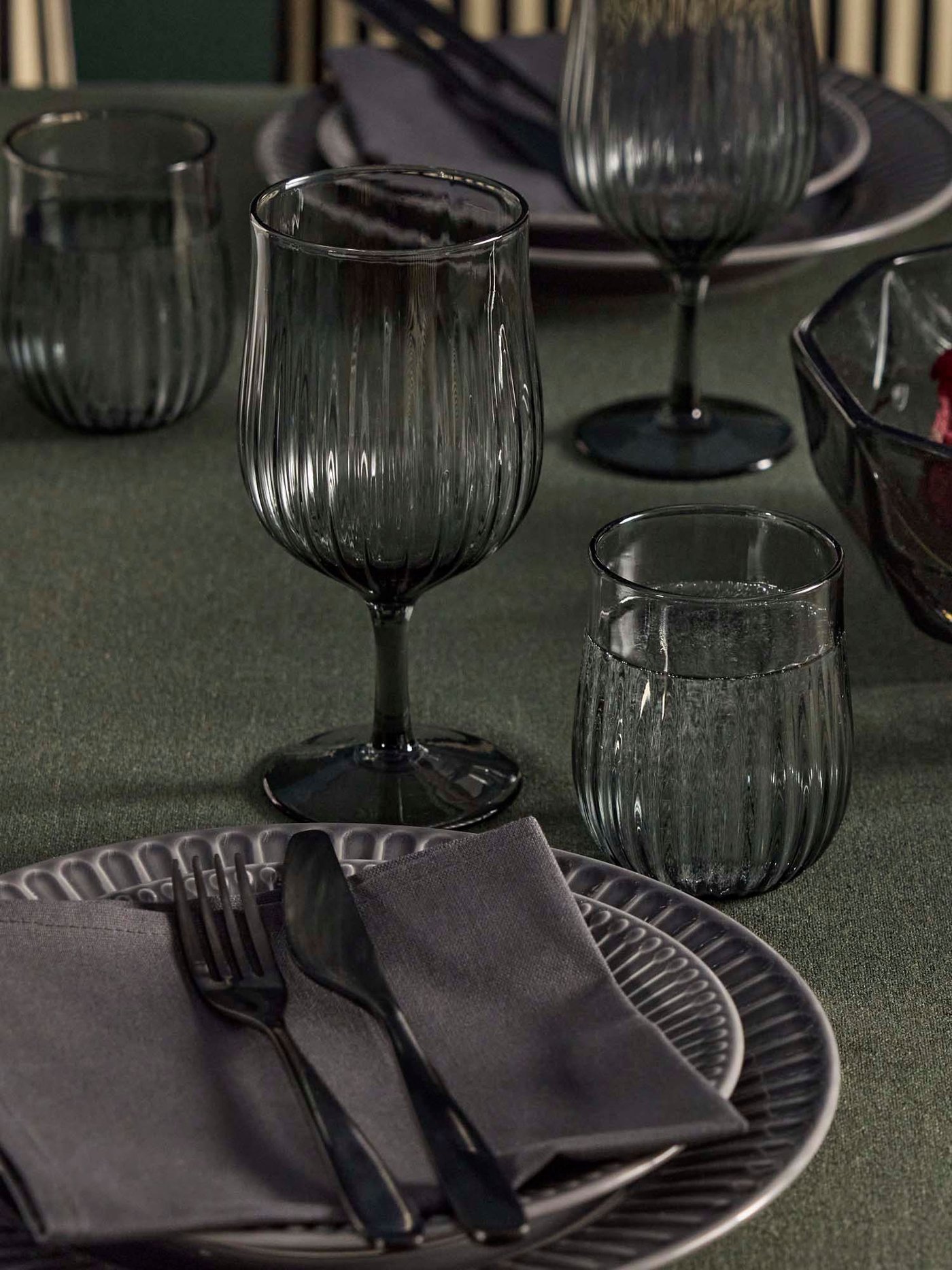 A table with grey stoneware STRIMMIG plates, HÖSTAGILLE glasses, wine glasses, and TILLAGD 24-piece cutlery.