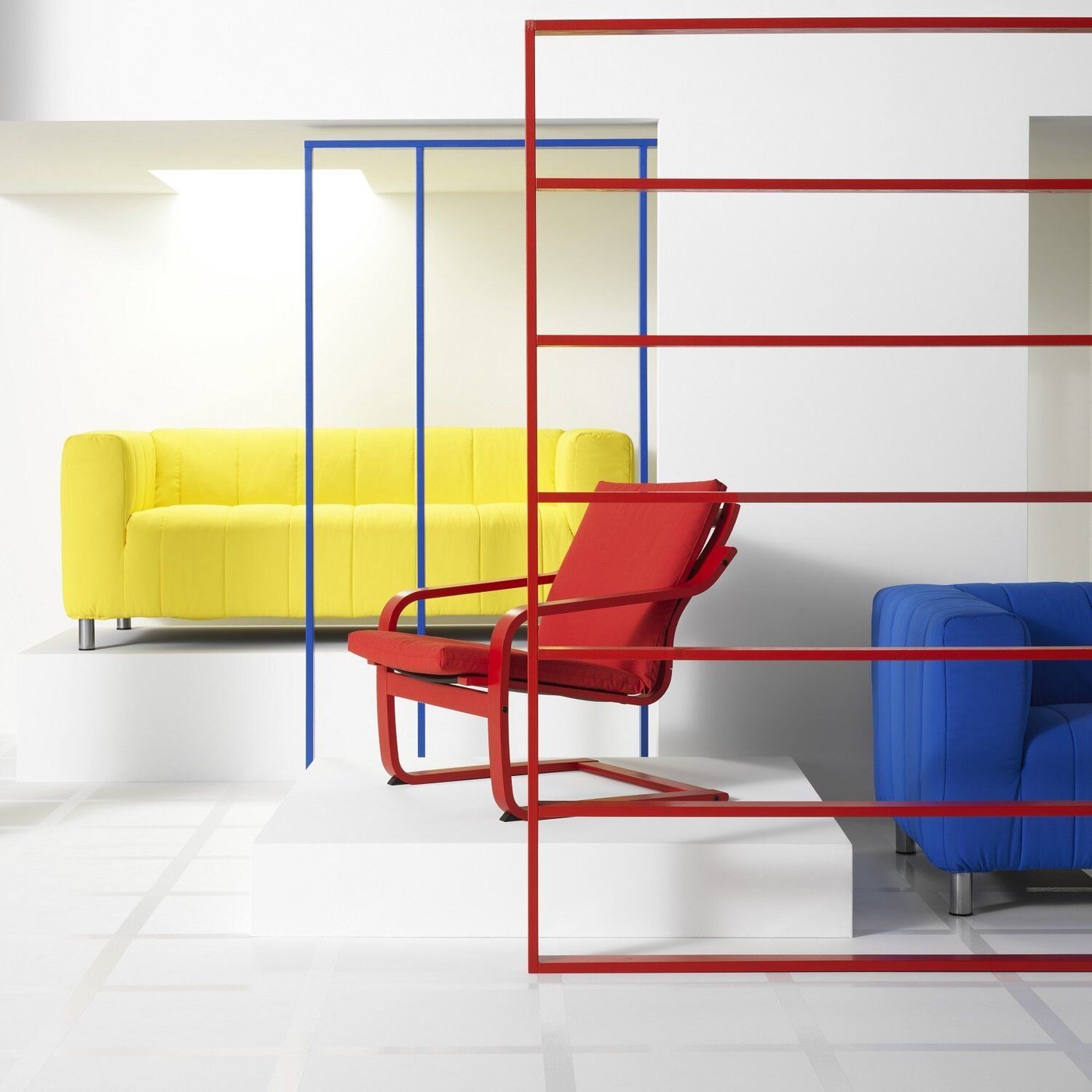 A red POÄNG char stands on a podium in front of a yellow KLIPPAN sofa in a white room. To the, right is the edge of a blue KLIPPAN sofa, standing in front of red stripe graphic elements.