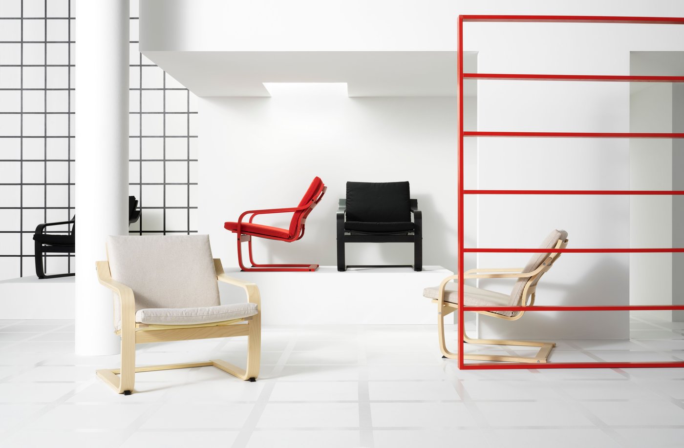 POÄNG chairs in different colours are standing on a podium in the back of a room. In front, two white POÄNG chairs are standing to face the camera. Red striped elements in the picture, to the right.