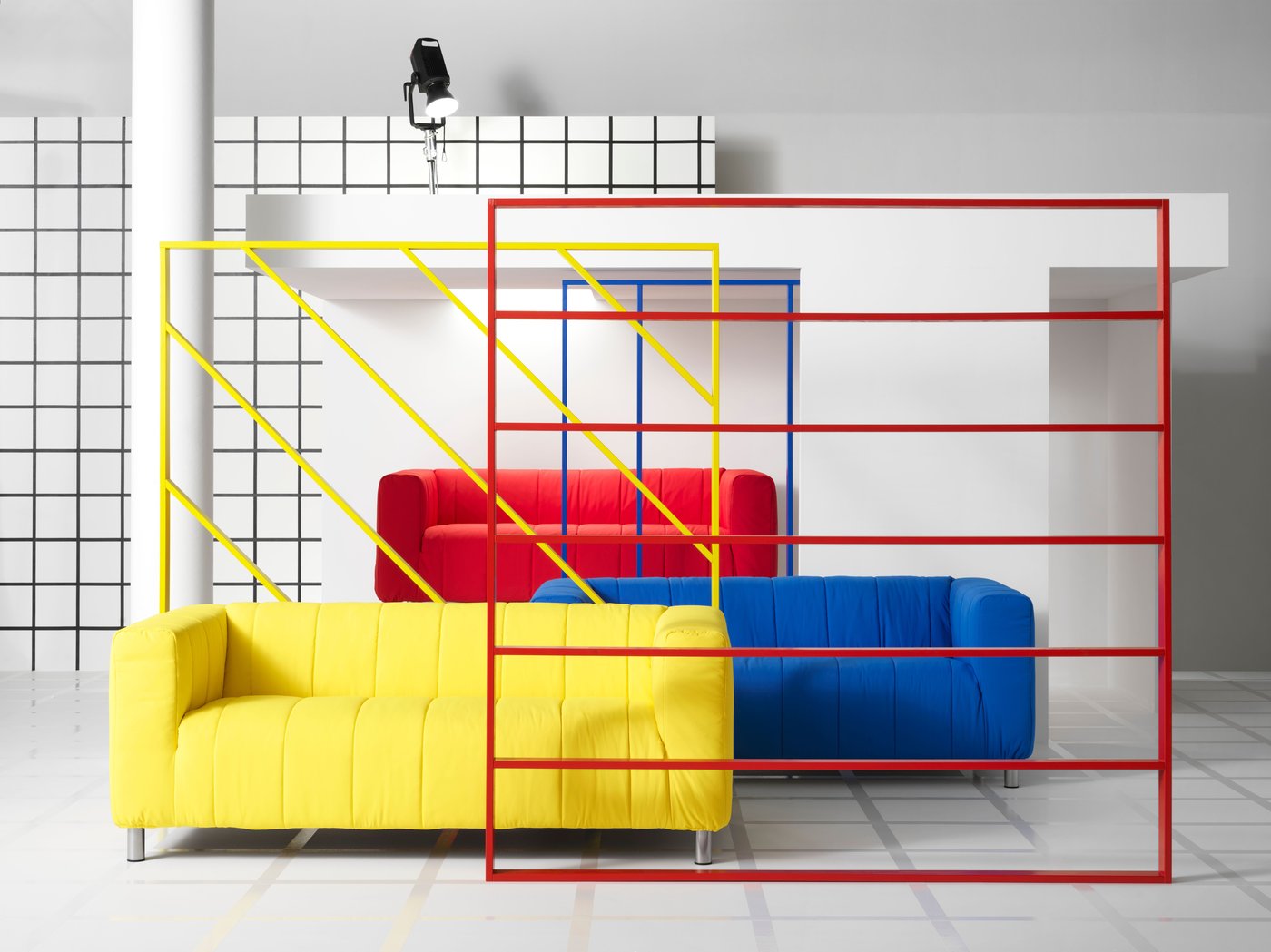 A roomset with three KLIPPAN sofas in red, blue and yellow, behind a red frame.