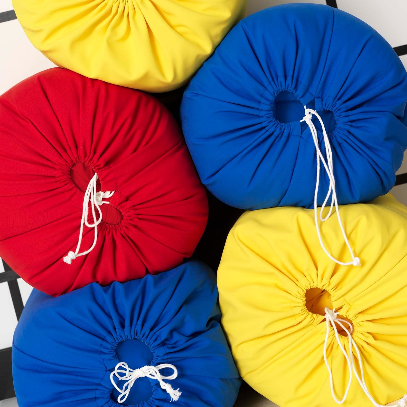 Five KLIPPAN sofa covers in yellow, red and blue drawstring duffle bags are stacked.