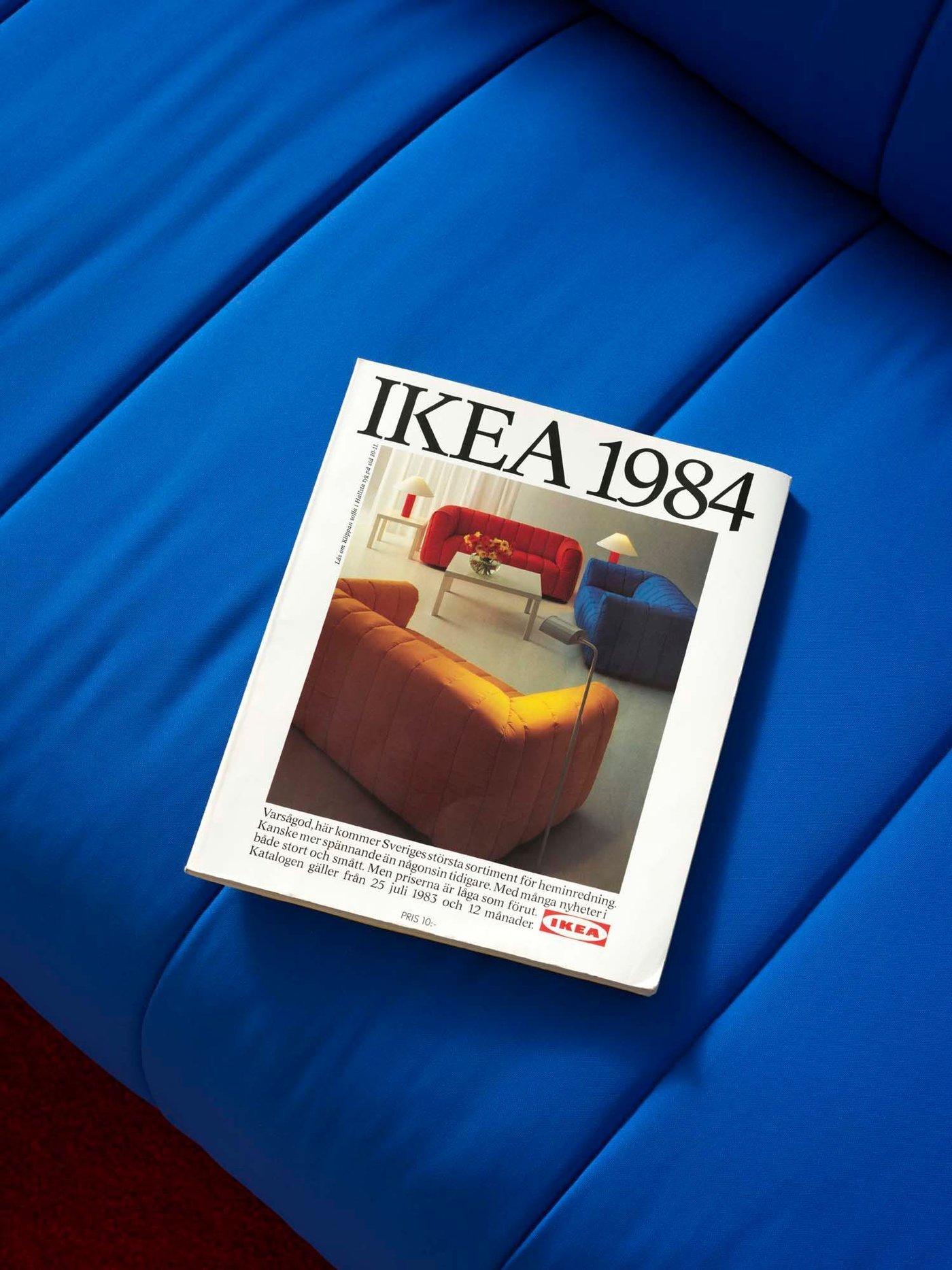 A 1984 IKEA catalogue lays on a blue KLIPPAN sofa. The cover has an image of three KLIPPAN sofas.