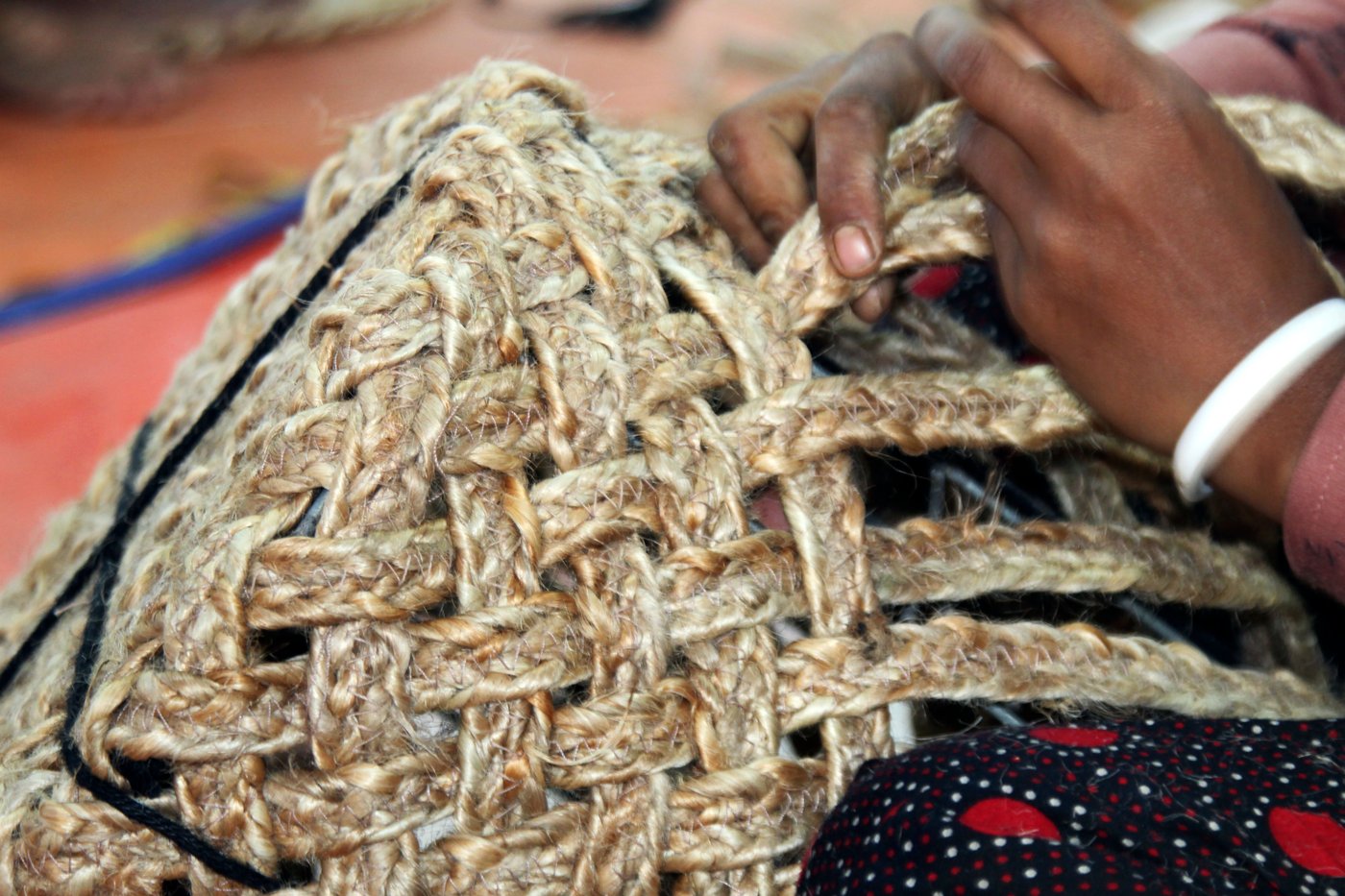 The image shows a woman's hand is working on a woven basket of natural fiber. 