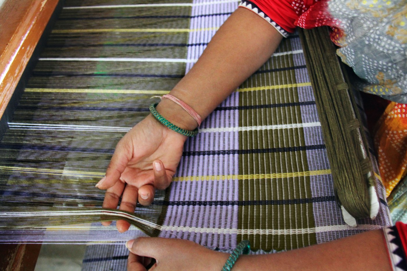 The image shows a woman's hand is working on a woven rug in colorful stripes.
