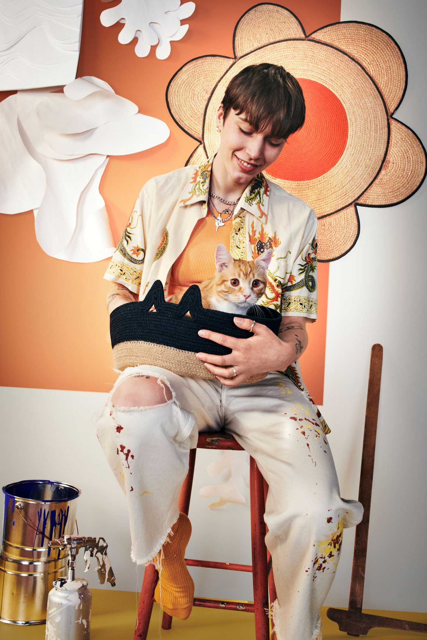 A young person sitting on a high stool is holding a woven basket from this collection, and in the basket there is a yellow-white cat.