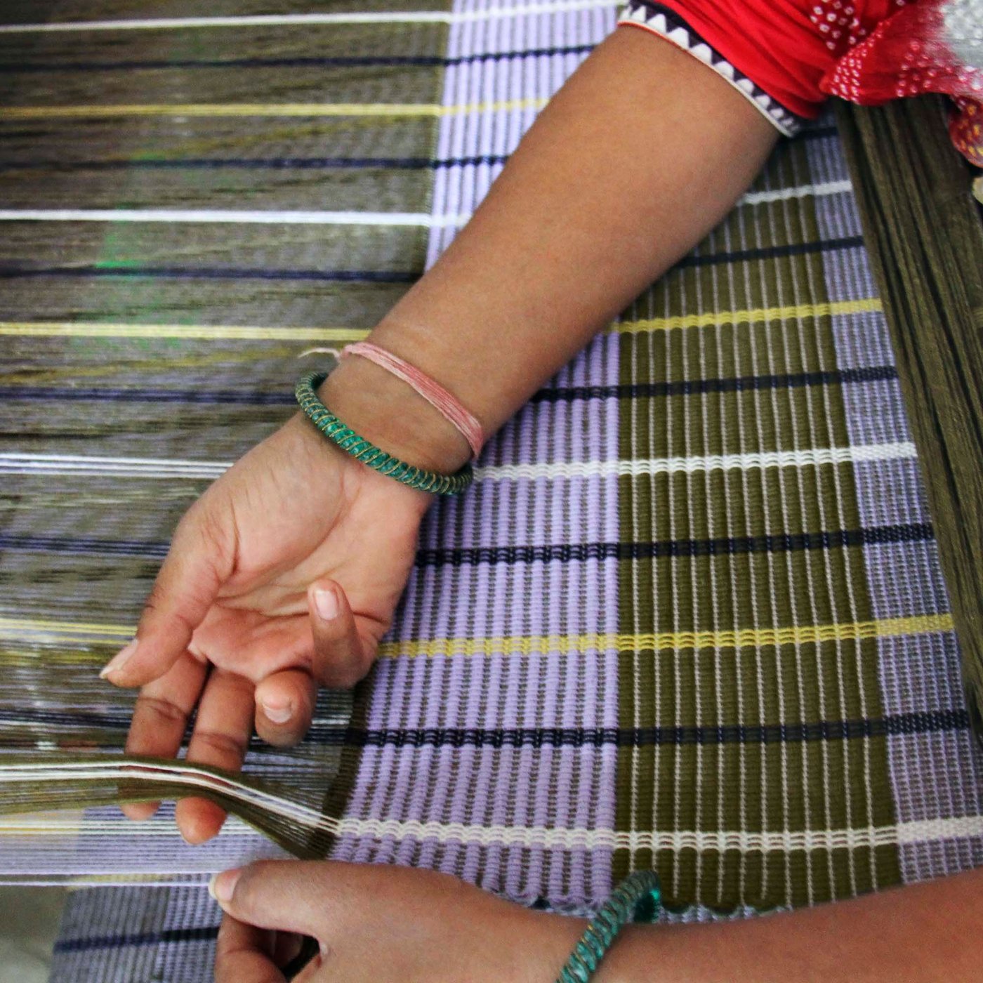 A pair of hands weaving a striped multicolour MÄVINN rug.