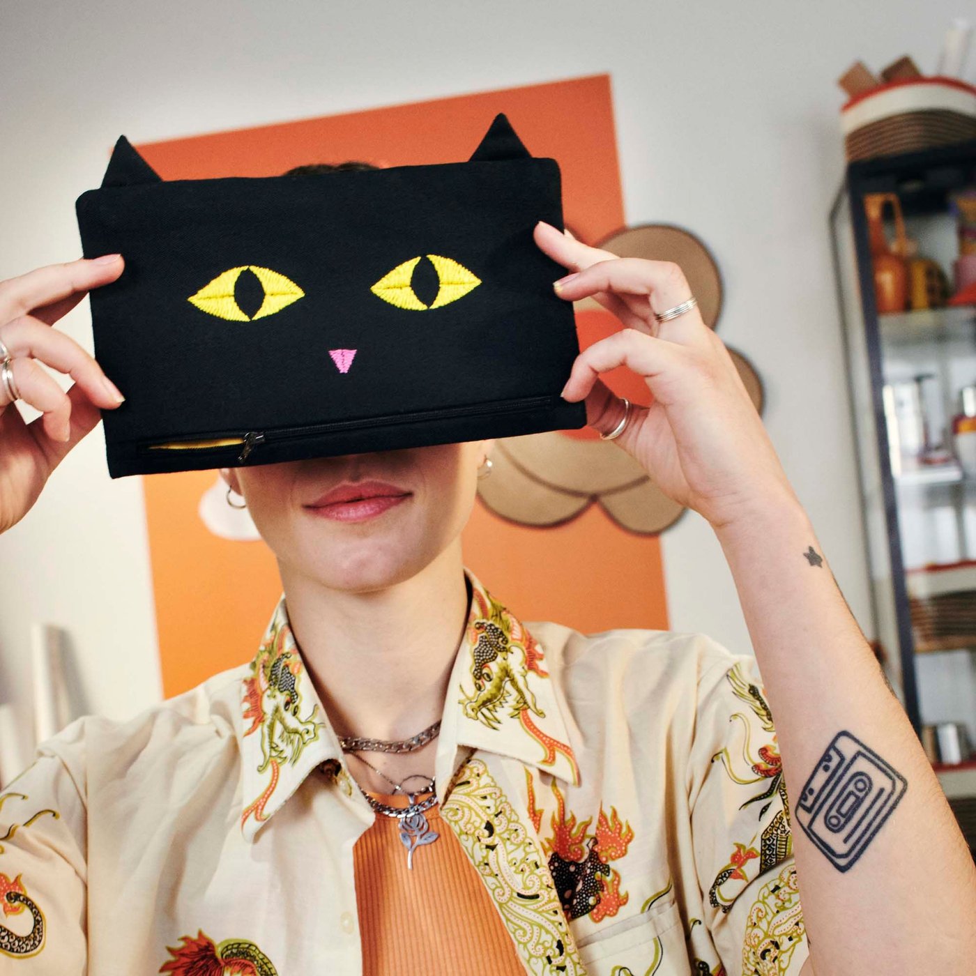 A woman holds a black bag with a cat face (from the MÄVINN collection) over her eyes, so she looks like she has cat eyes.