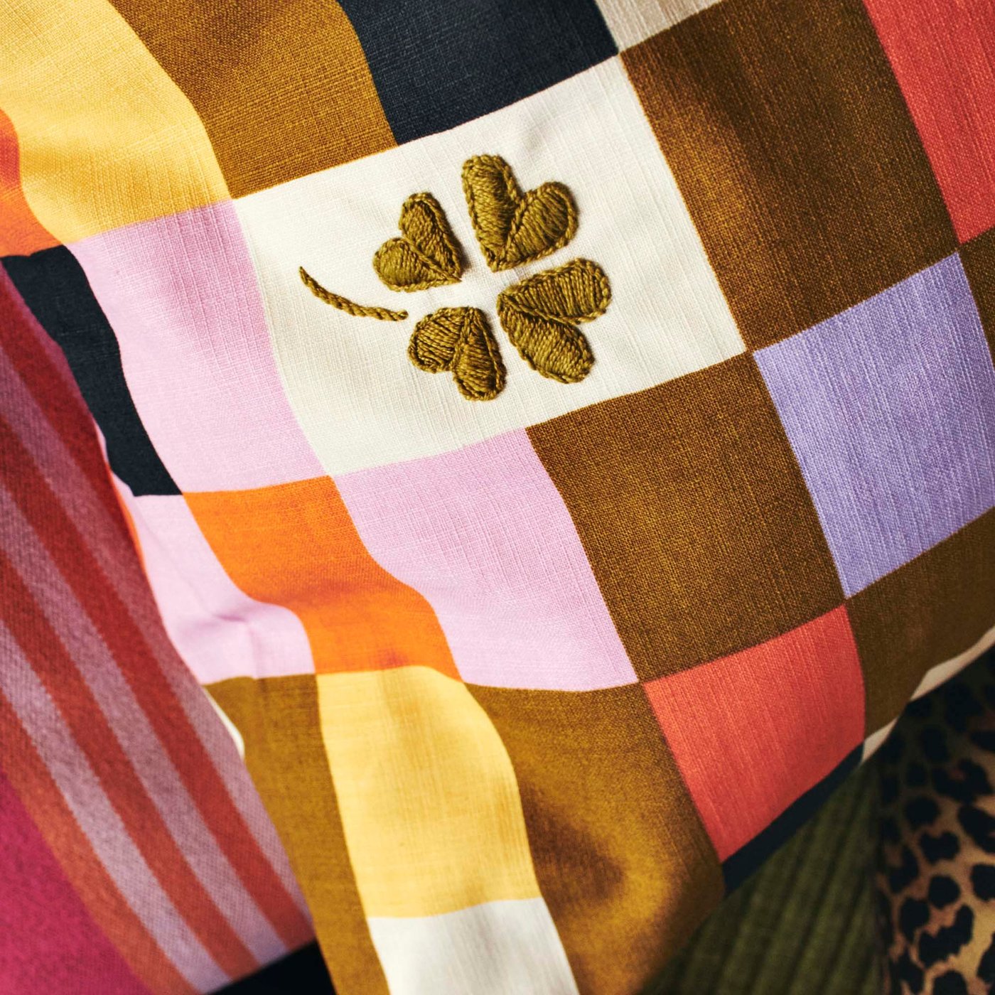 A closeup on an embroidered four-leaf clover on a check pattern multicolour MÄVINN cushion cover.