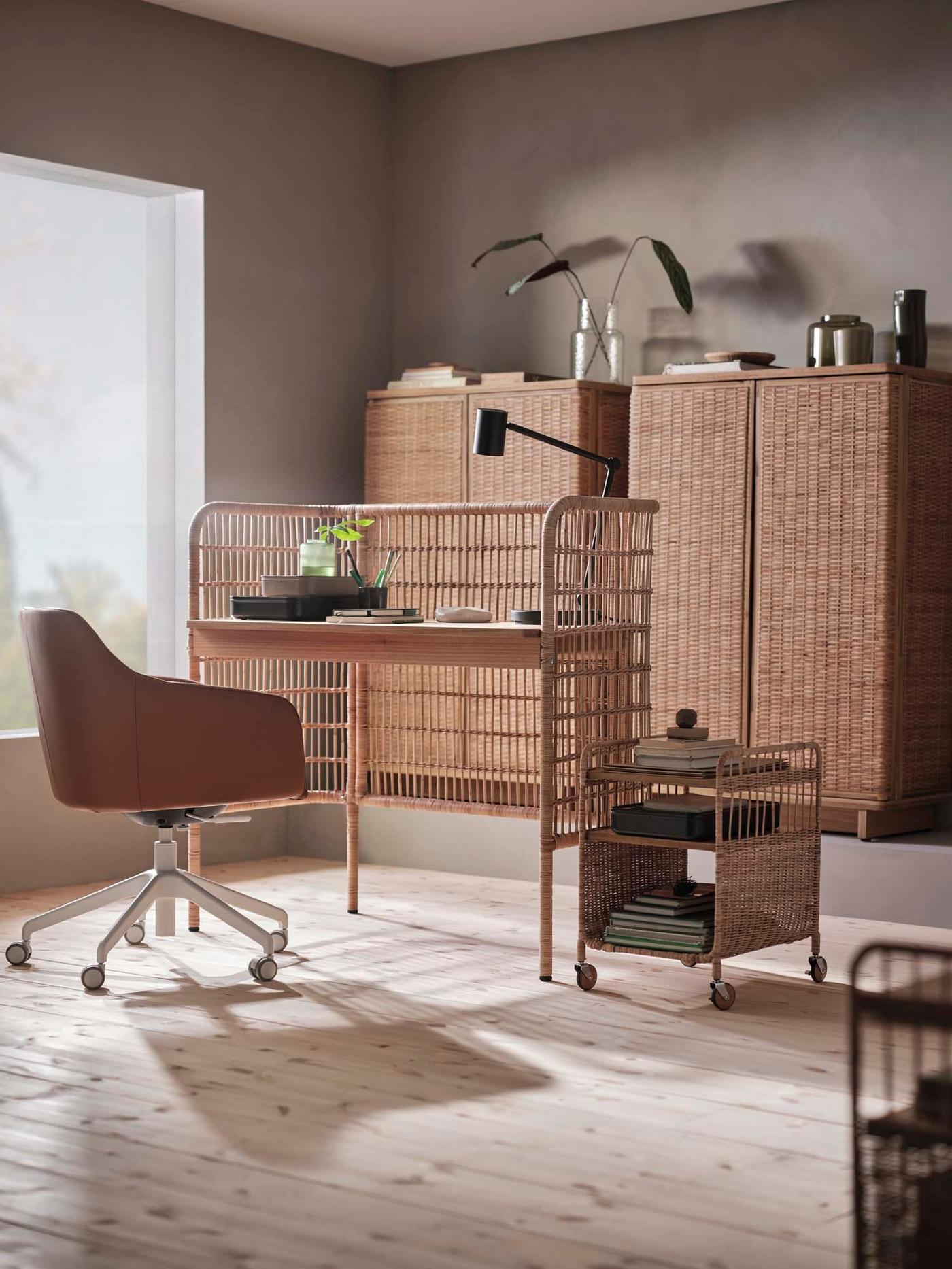 A home office roomset, with a FRYKSÅS rattan desk in the centre, surrounded by an office chair, low storage unit on weels and rattan cabinets in the background. Light shines in from the window.