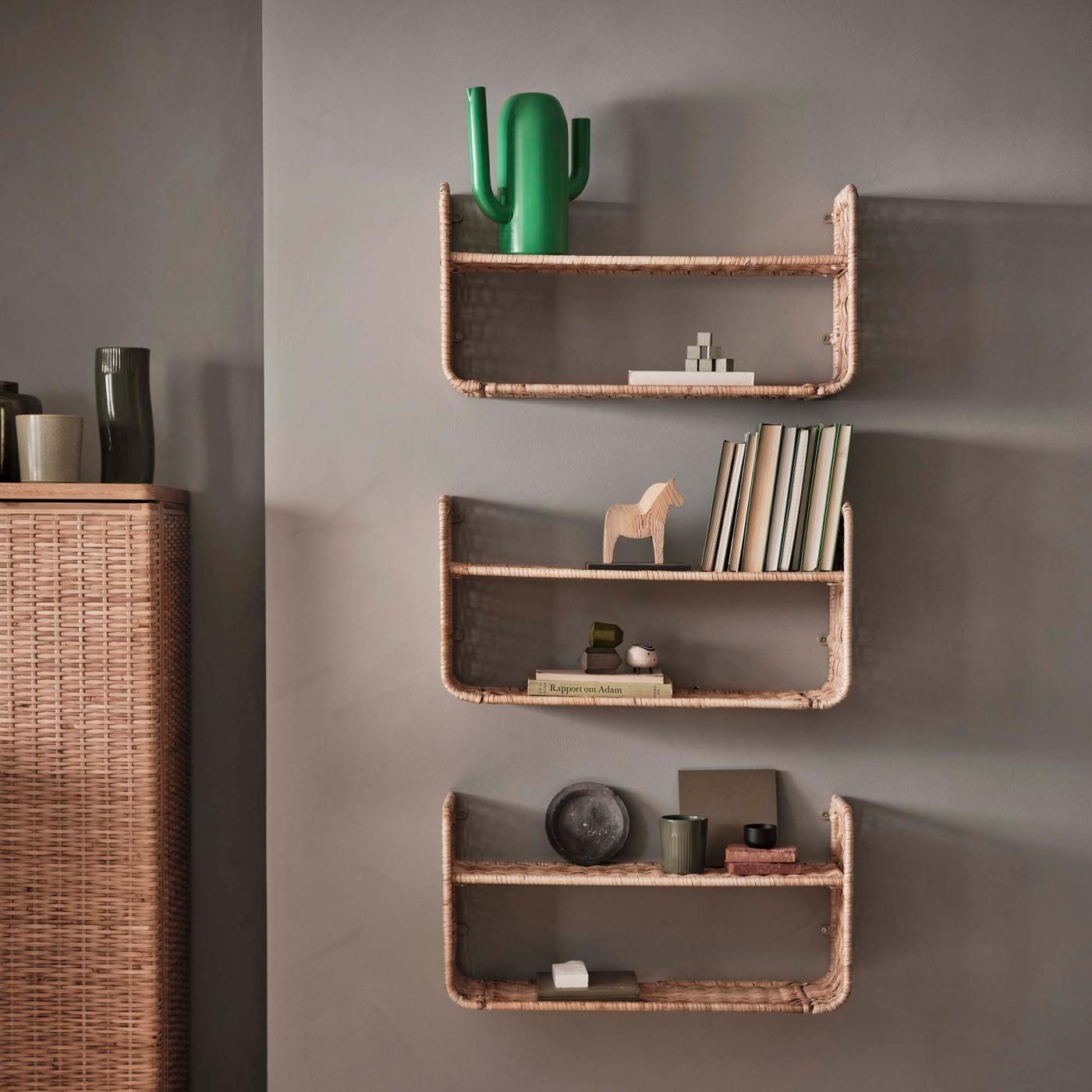 A taupe coloured wall with three rattan shelves in a column and a storage unit to the left. There are books and ornaments on the shelves.