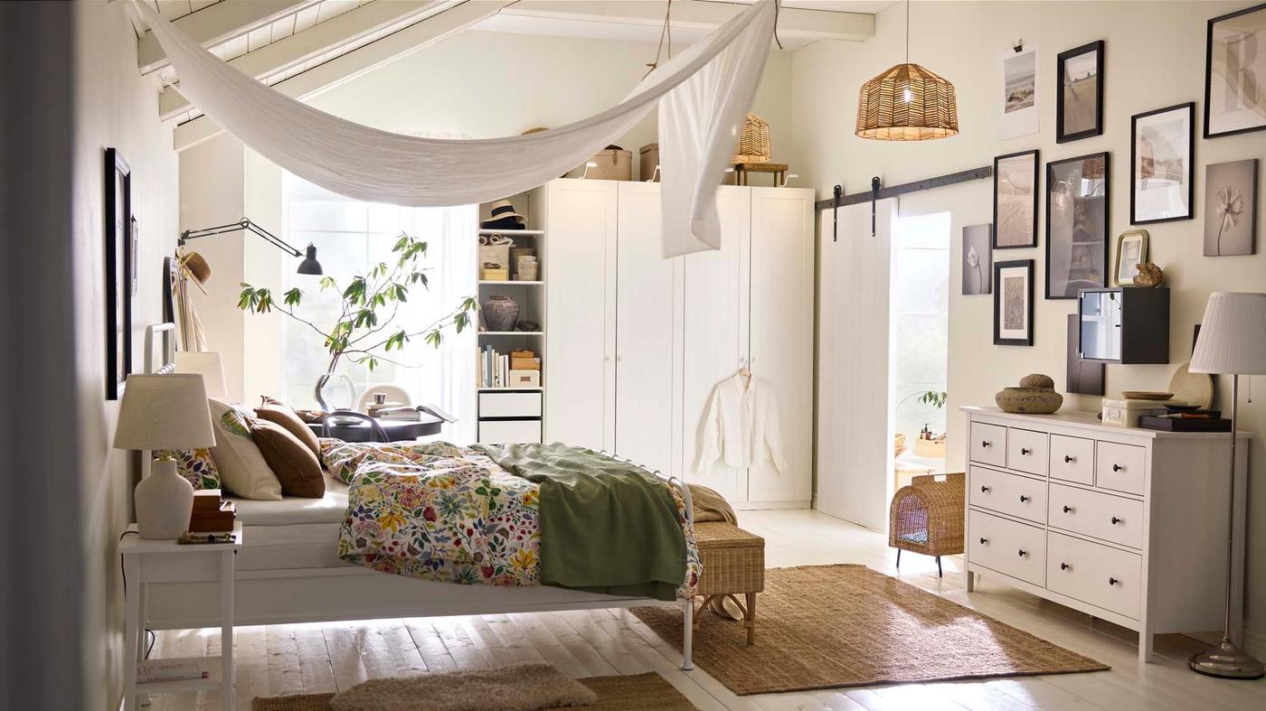 A white bedroom with wardrobes, a bed with a floral cover and a canopy above.