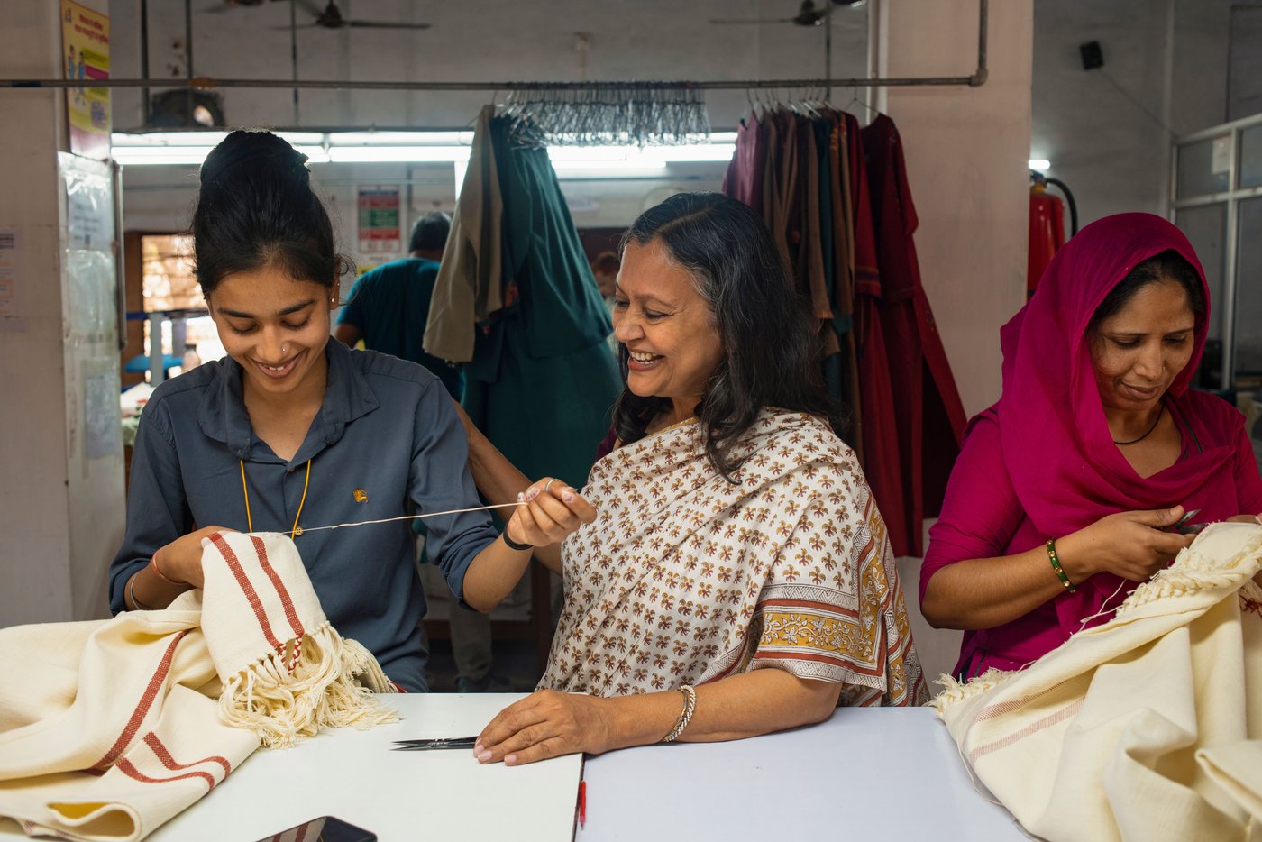Three southeast Asian women dressed in traditional outfit are working with handcrafted work. They all look happy and smiley in the picture.