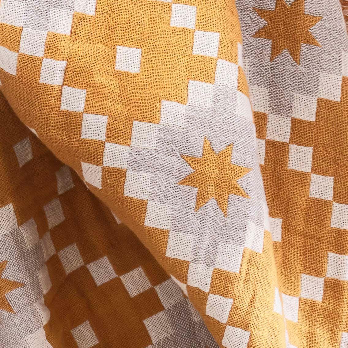 A close-up of a yellow and beige patterned SVARTFRYLE throw with pixelated squares with squares and stars in the centre of each square.