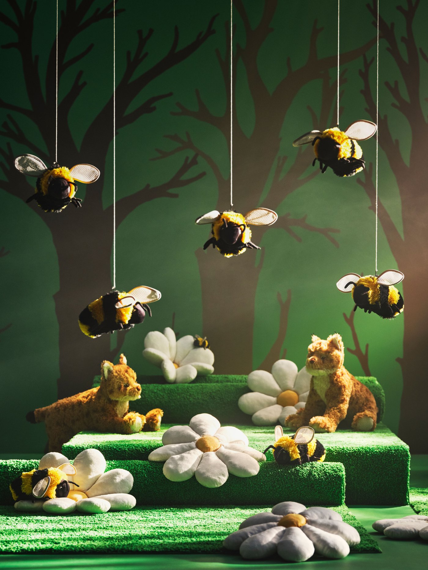 Fluffy bee- and wildcat soft toys from the SKOGSDUVA collection sit among giant daisies against a painted forest backdrop.