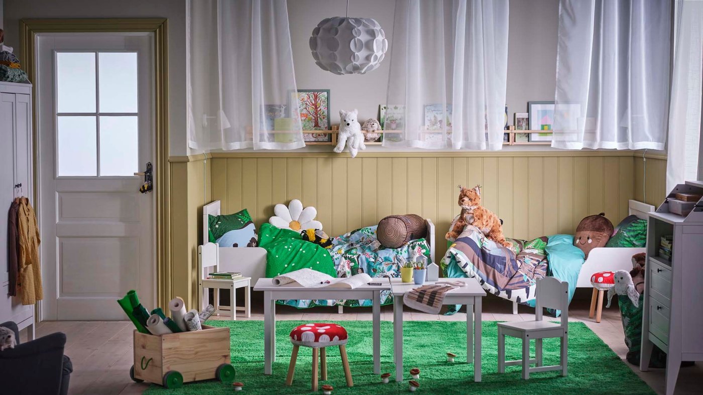 A bedroom with two SUNDVIK extendable beds with SKOGSDUVA bedding behind two white tables and SUNDVIK children's chairs.