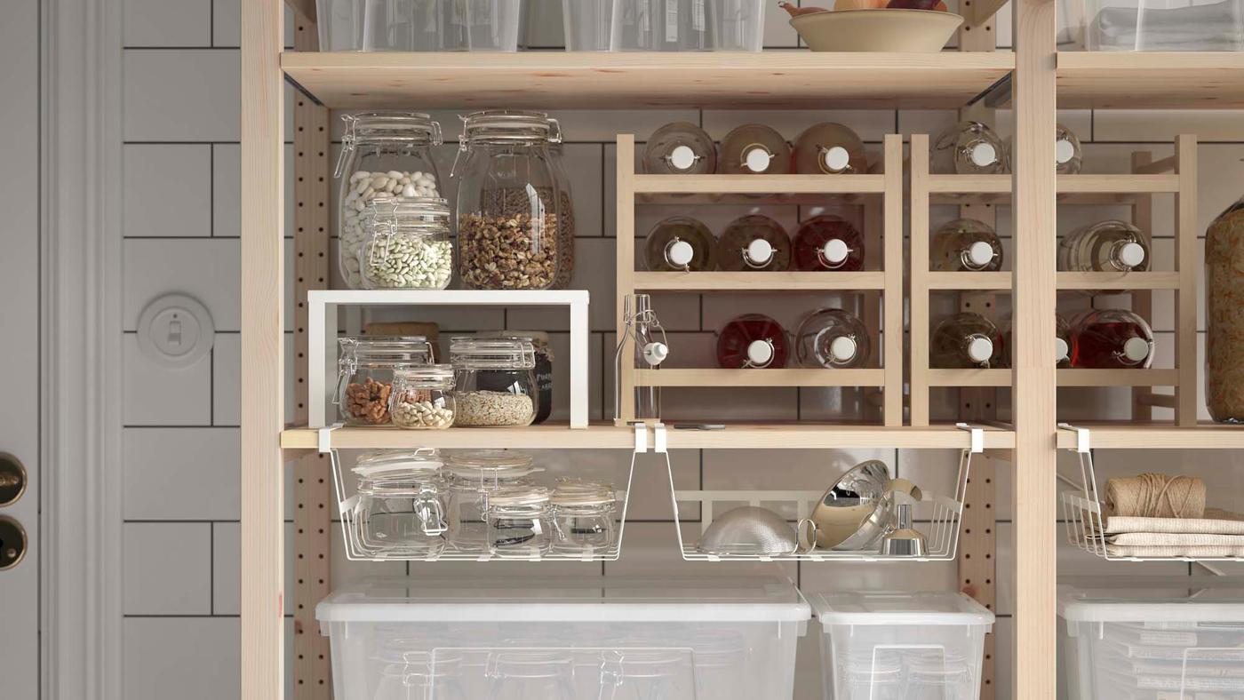A wooden shelving unit filled with neatly stored food and bottles of liquid against a white wall.
