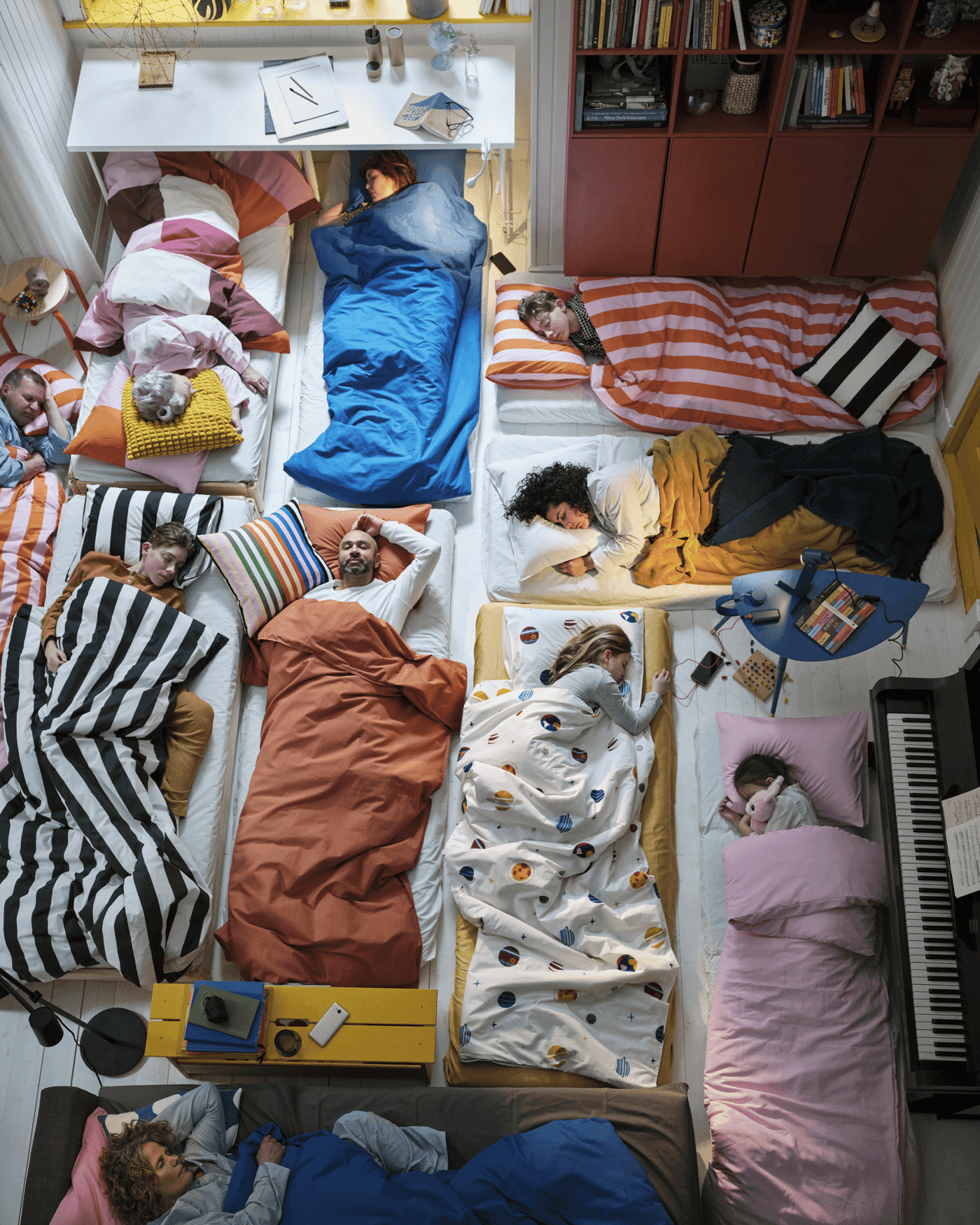 shot from above, people of various ages lying in different beds with different beddings and colours, sleeping next to each other
