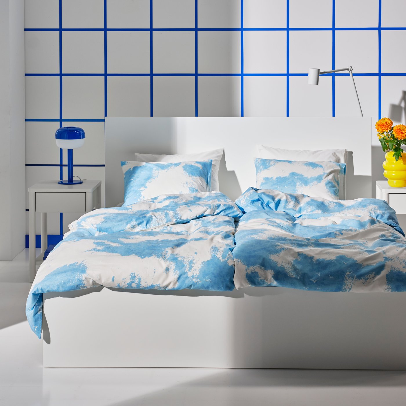 The image shows a set of new items from the 6th drop of Nytillverkad collection, including a double sized bed with a bed linen set with the pattern of blue sky and white clouds..