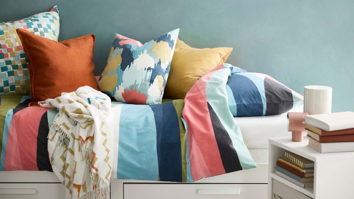 Solid and patterned coloured cushions match the colourful striped SVALSTJÄRTAR duvet cover on a HEMNES day bed.